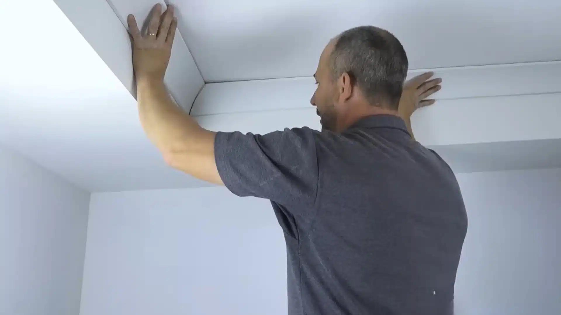 man dry fitting crown molding piece into corner by pressing it firmly against ceiling with two hands