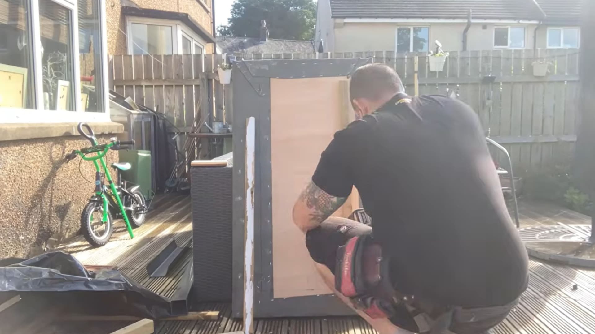 man fitting a plywood cladding panel onto the side of a grey felt roofed structure
