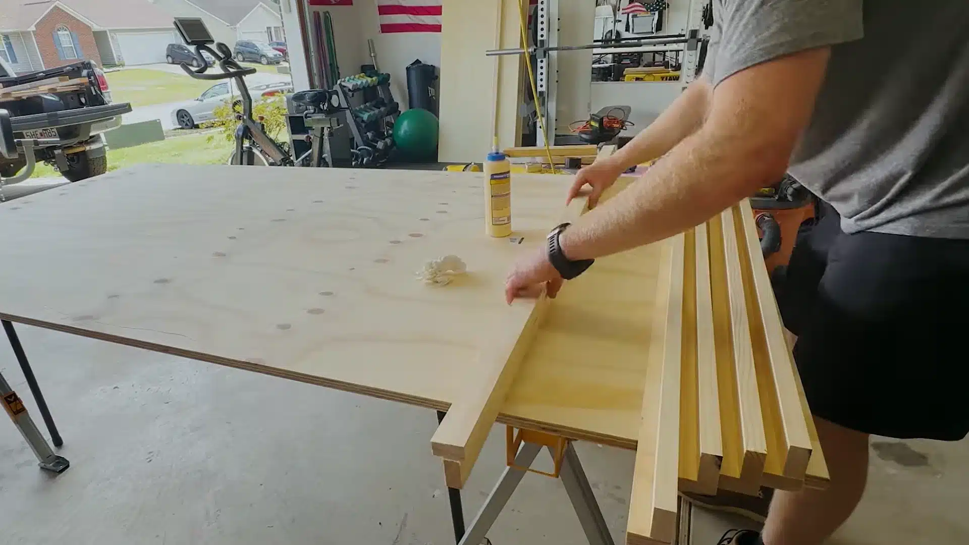 man gluing and clamping wooden strut pieces together on a garage workbench surface