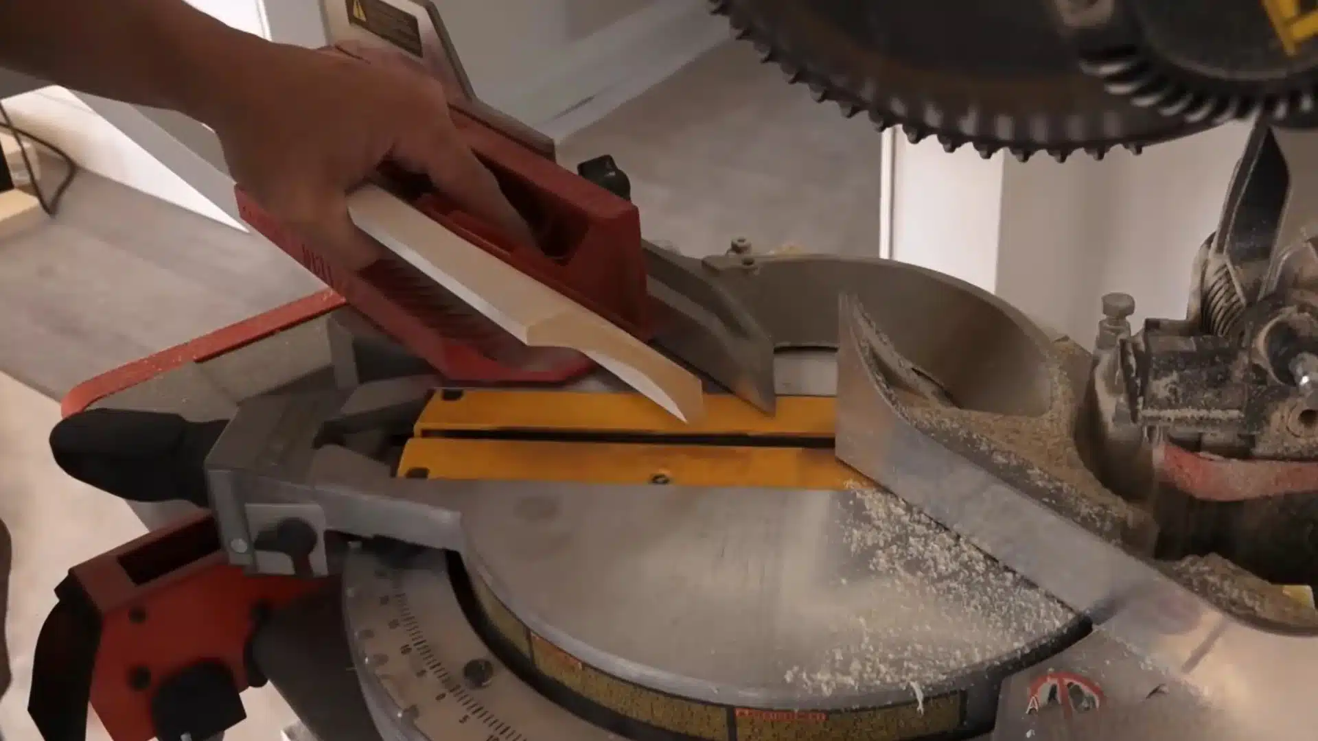 man holding piece of crown molding trim against a miter saw blade before making an angled corner cut
