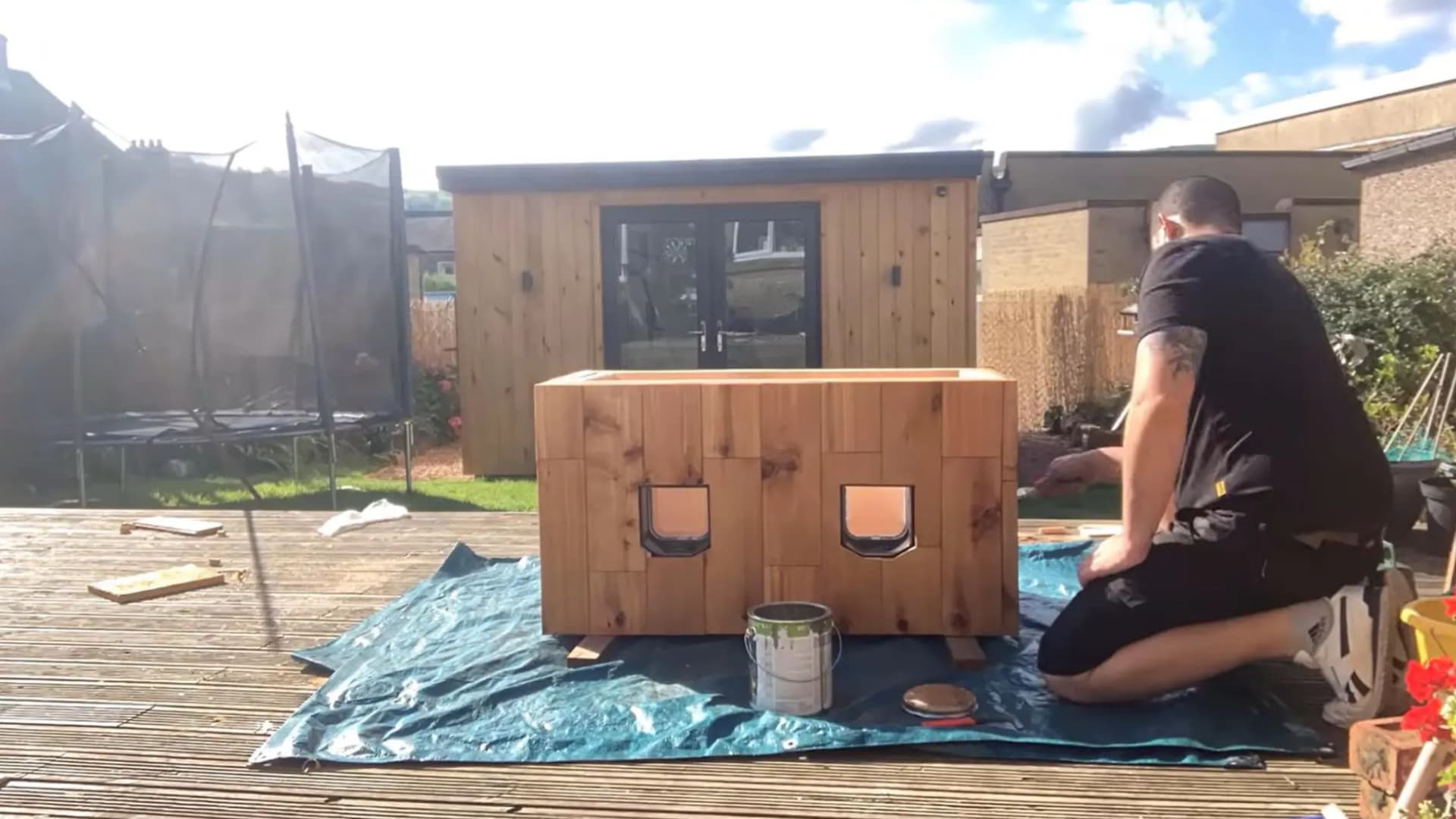 man kneeling beside a wooden cat house with two cat flaps fitted into the cladding