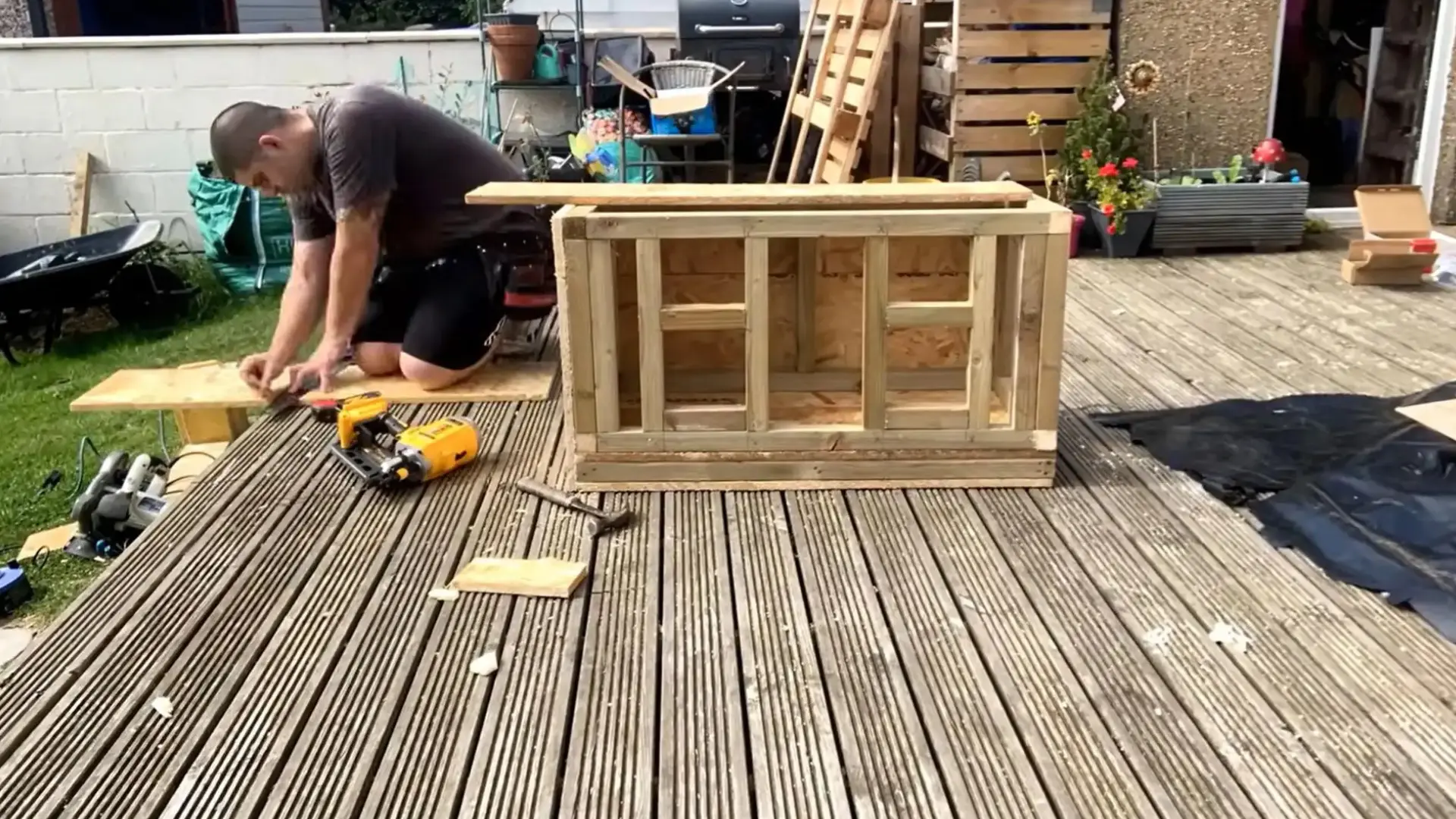 man kneeling to attach a wooden batten near a finished plywood box frame on decking
