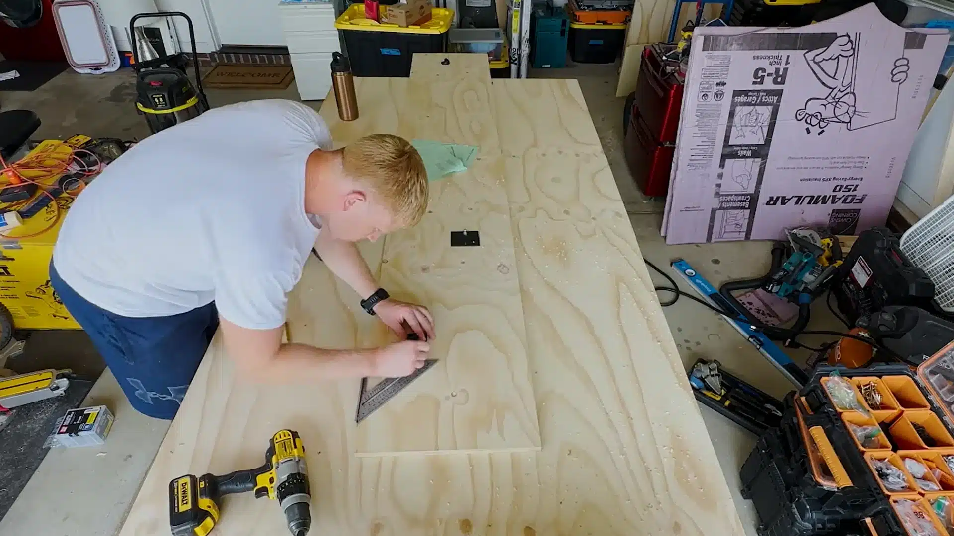 man marking a cut measurement on a plywood board with a square before cutting it