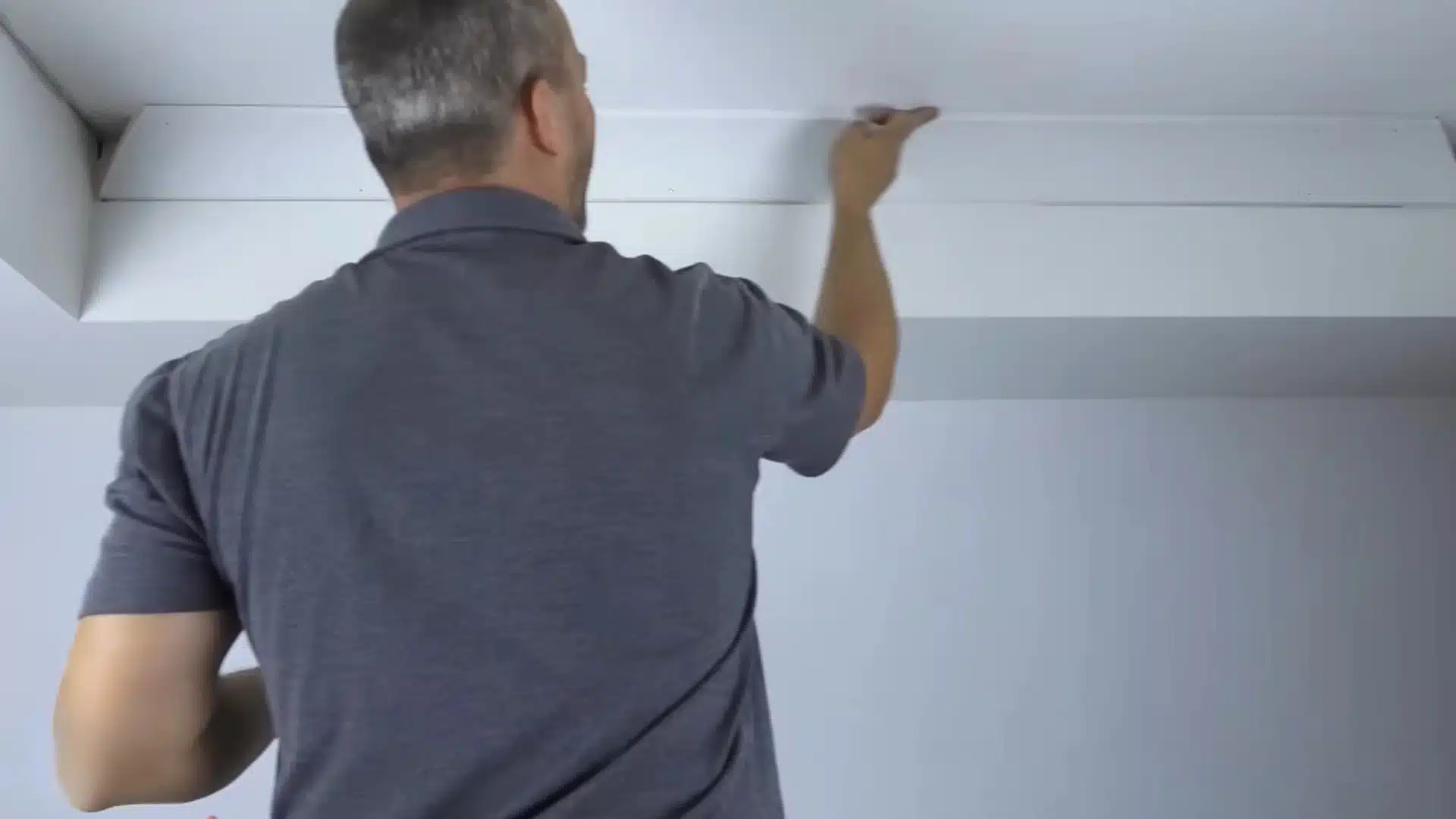 man pointing closely at an inside ceiling corner joint of crown molding checking for gaps and coping