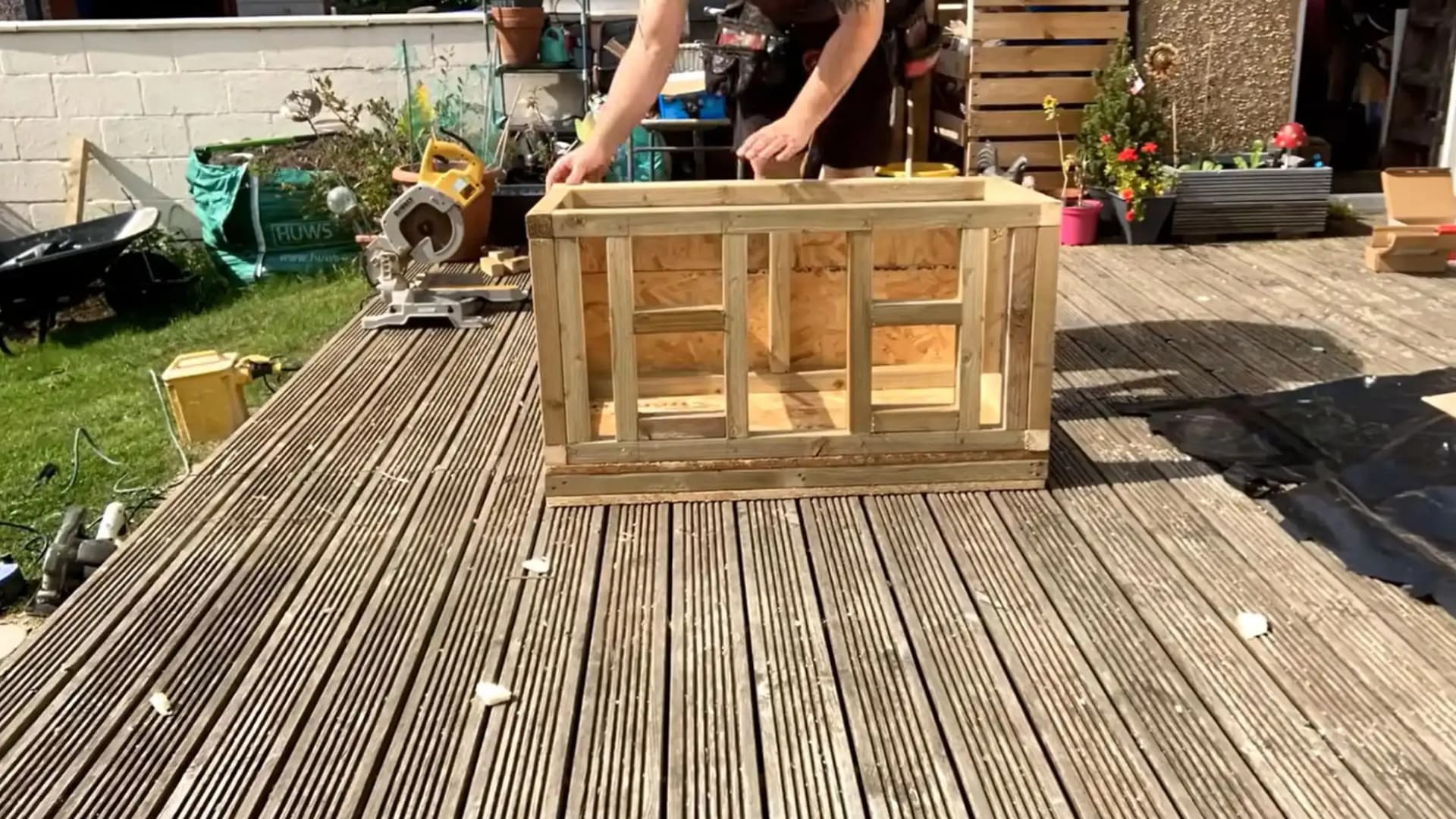 man reaching over a wooden box frame with osb panels covering the exterior side walls fully