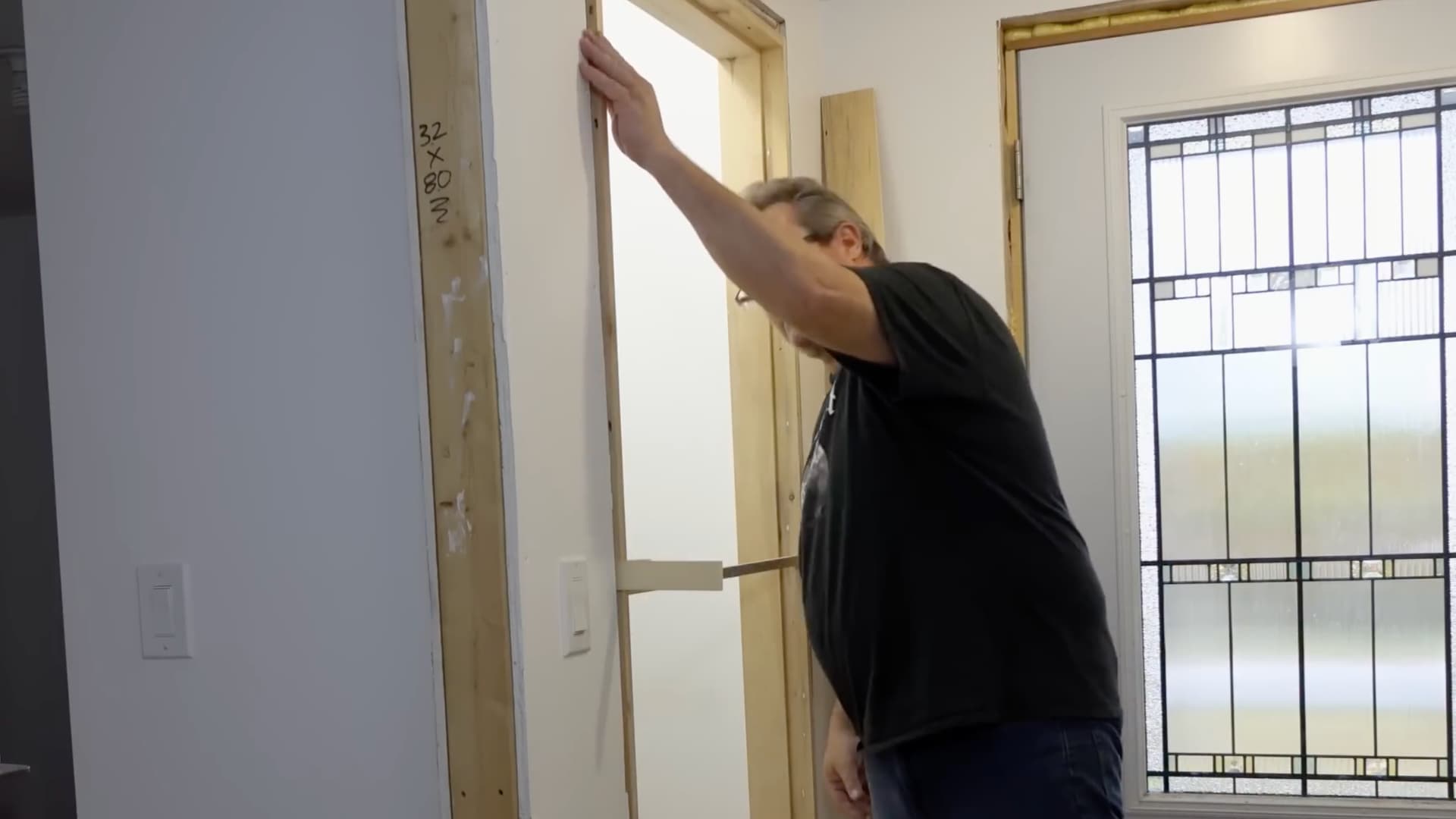 man reaching up to press door frame into opening with wood shim visible nearby
