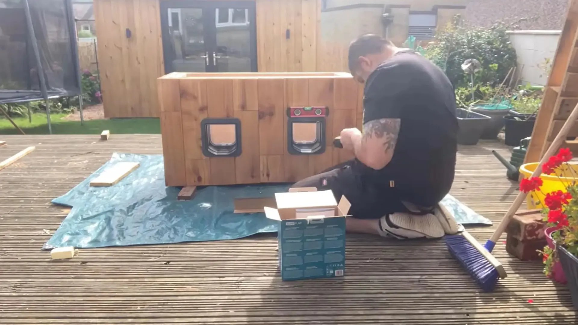 man screwing a cat flap into place on a finished wooden cat house with two entrances