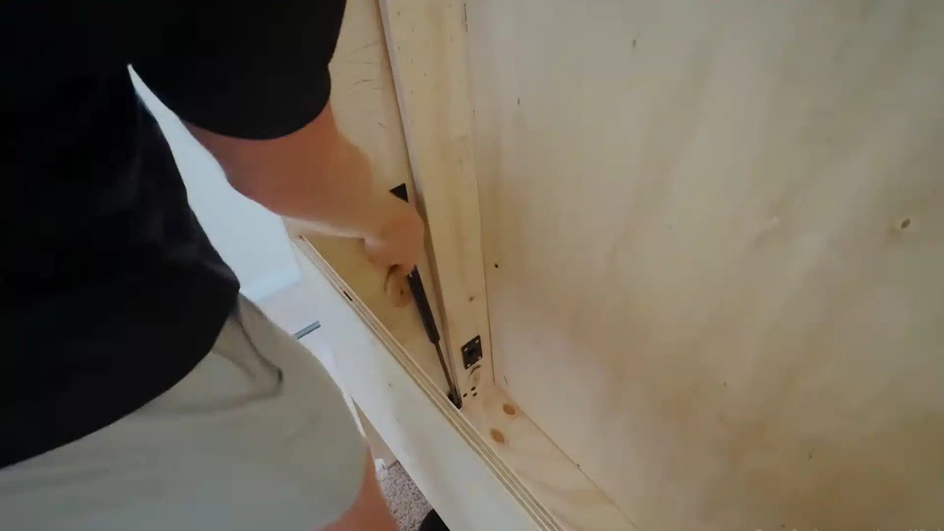 man screwing a hydraulic piston bracket onto the underside of a plywood bed panel