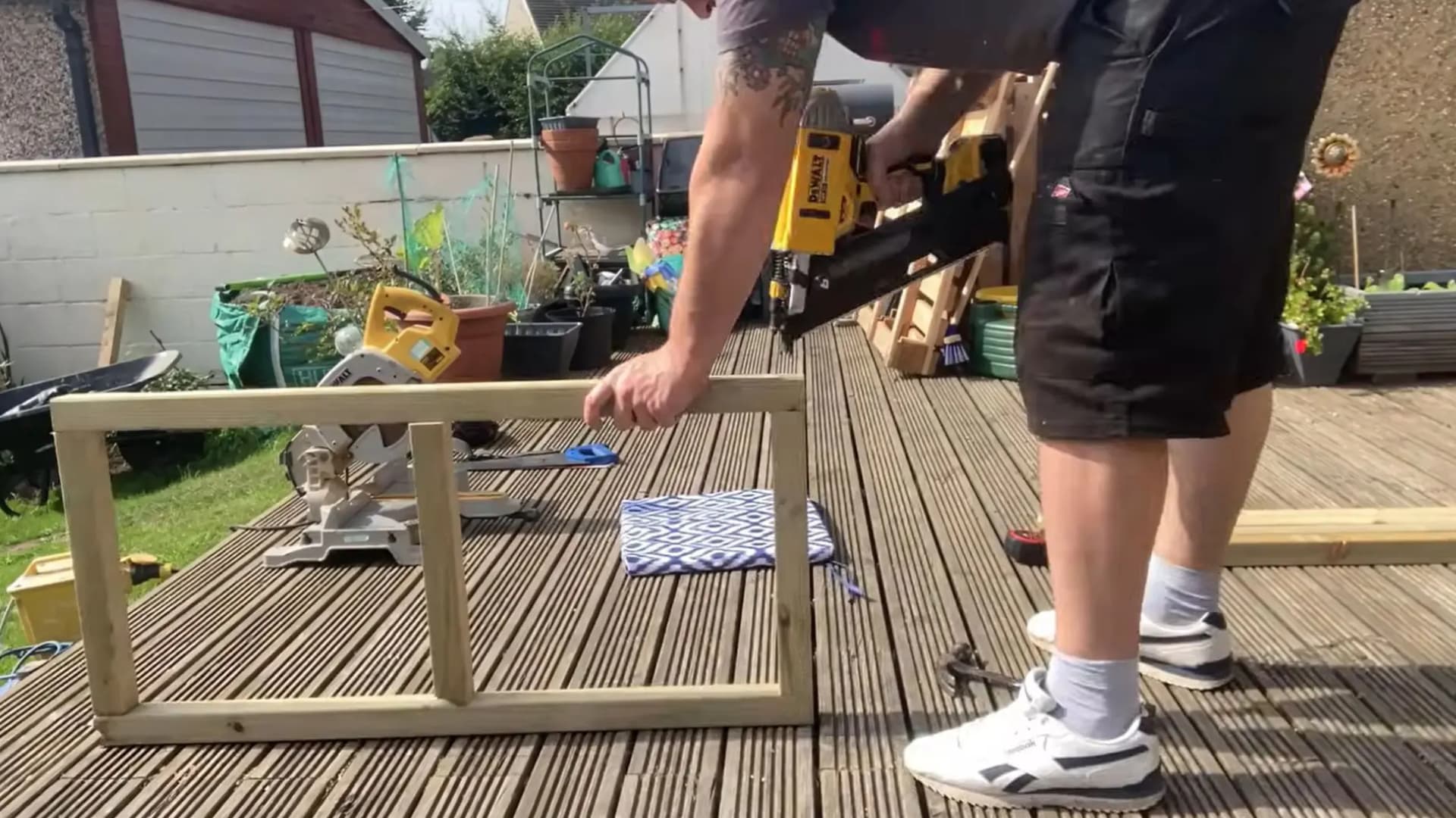 man using a yellow nail gun to join wooden base frame corners together on an outdoor deck