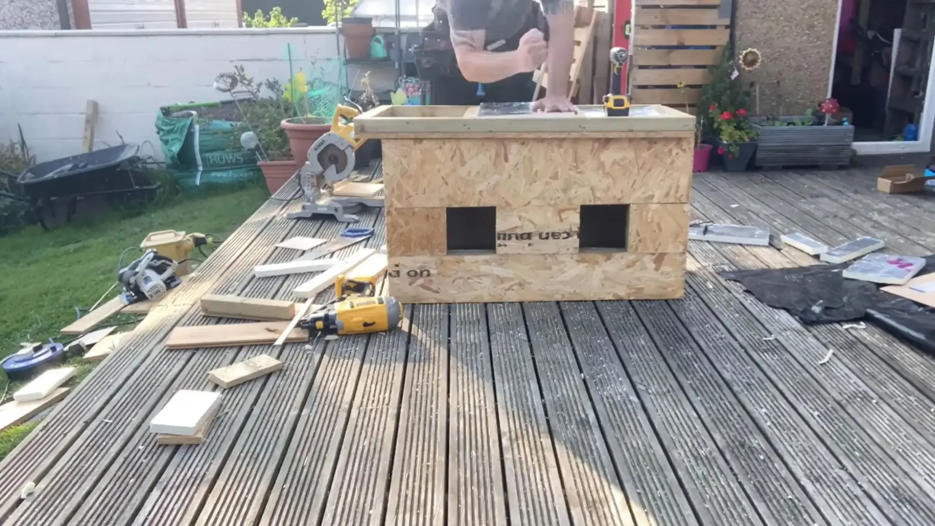 man working on top of an osb box structure that has two square entrance holes already cut