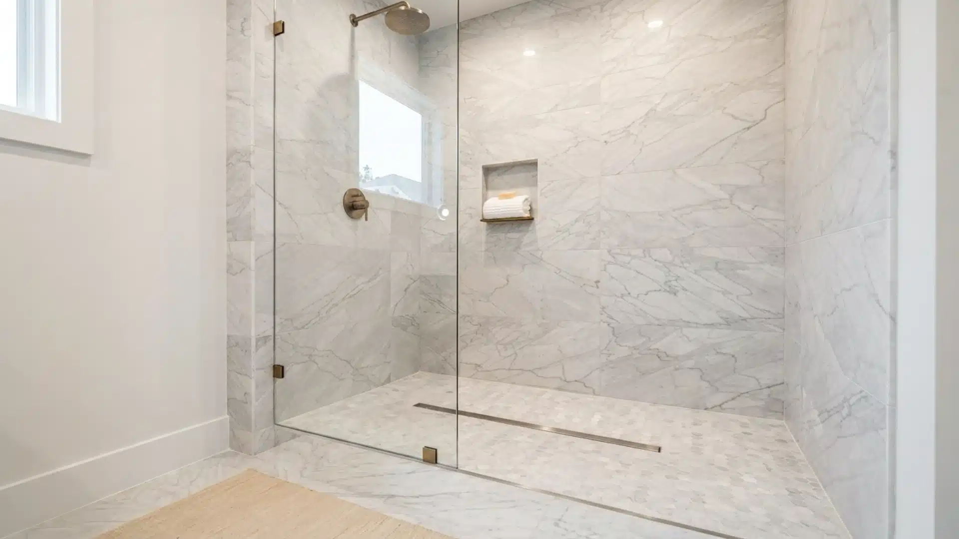 marble curbless shower with brass fixtures glass panel and niche holding folded towel