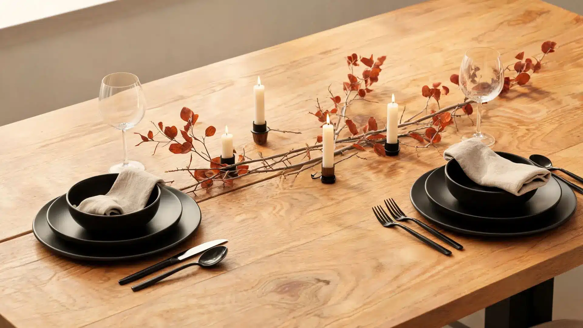 matte black dinnerware and black flatware on light wood, with autumn branches and taper candles