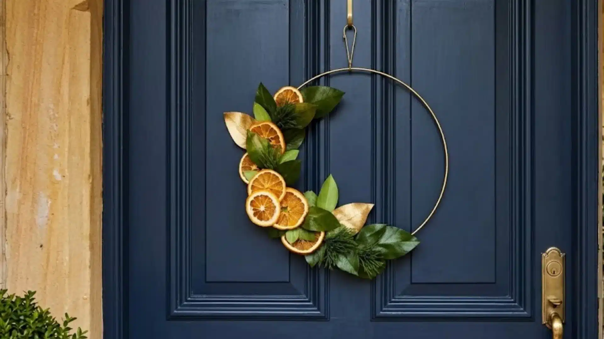 metal hoop wreath with dried orange slices and green leaves hanging on a dark blue front door