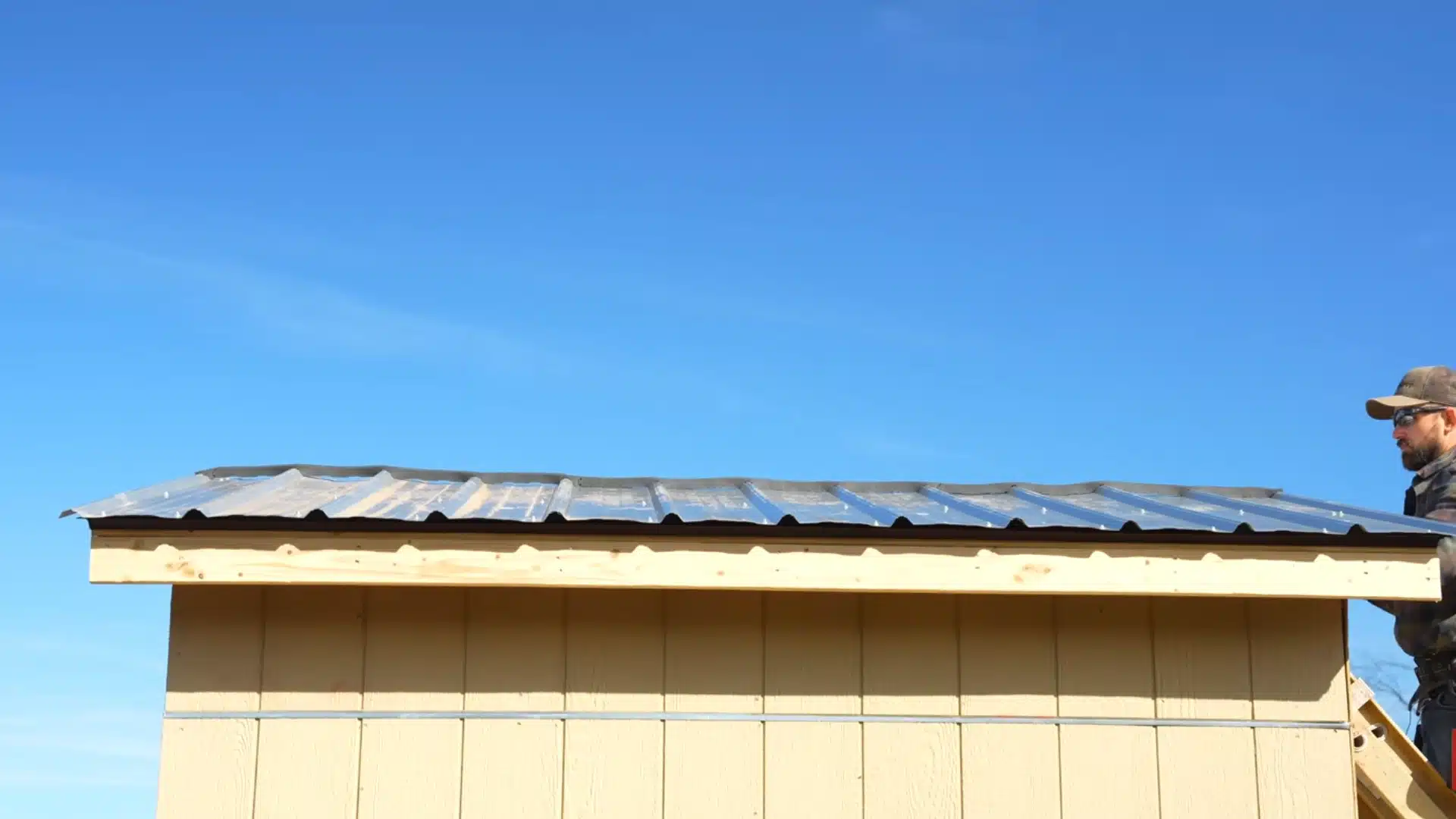 metal roof installation with panels being placed on trusses under clear blue sky
