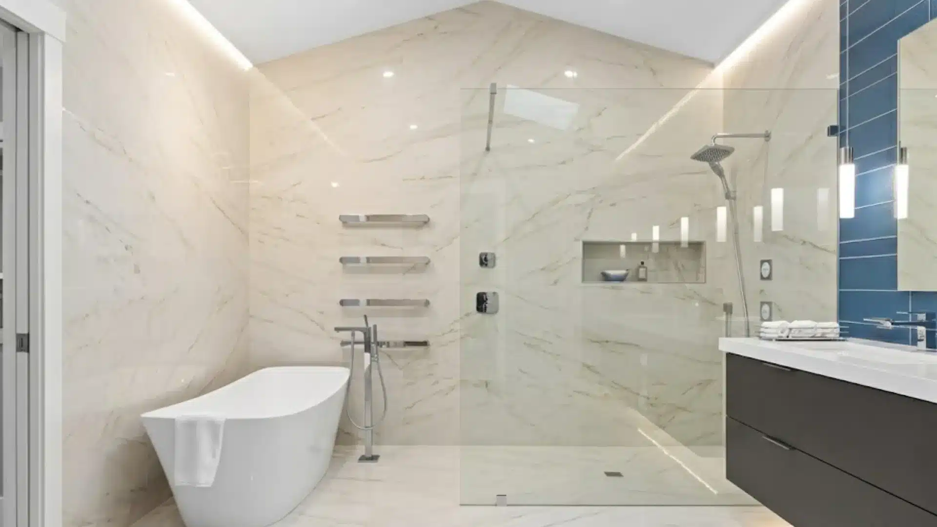 modern bathroom with beige marble tiles, a freestanding tub, glass shower, and dark vanity