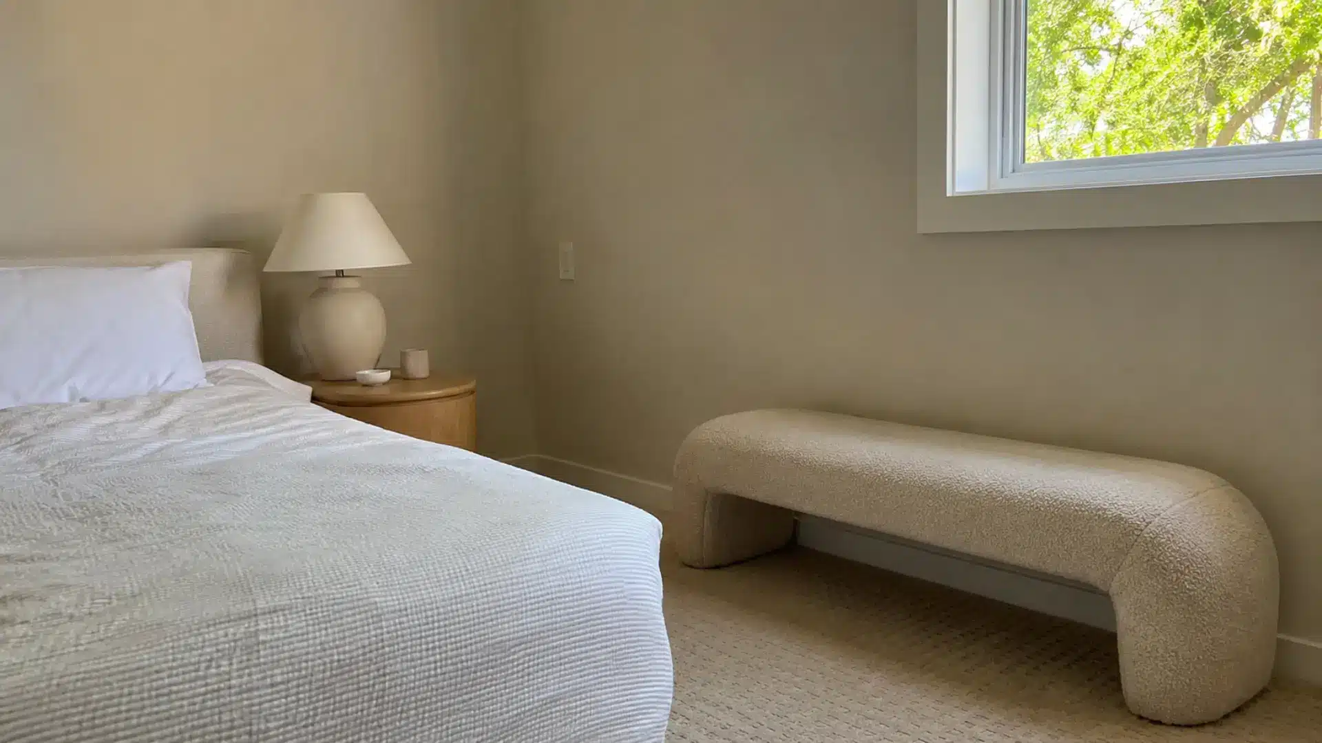 neutral bedroom with boucle bench, round nightstand, and textured beige carpet