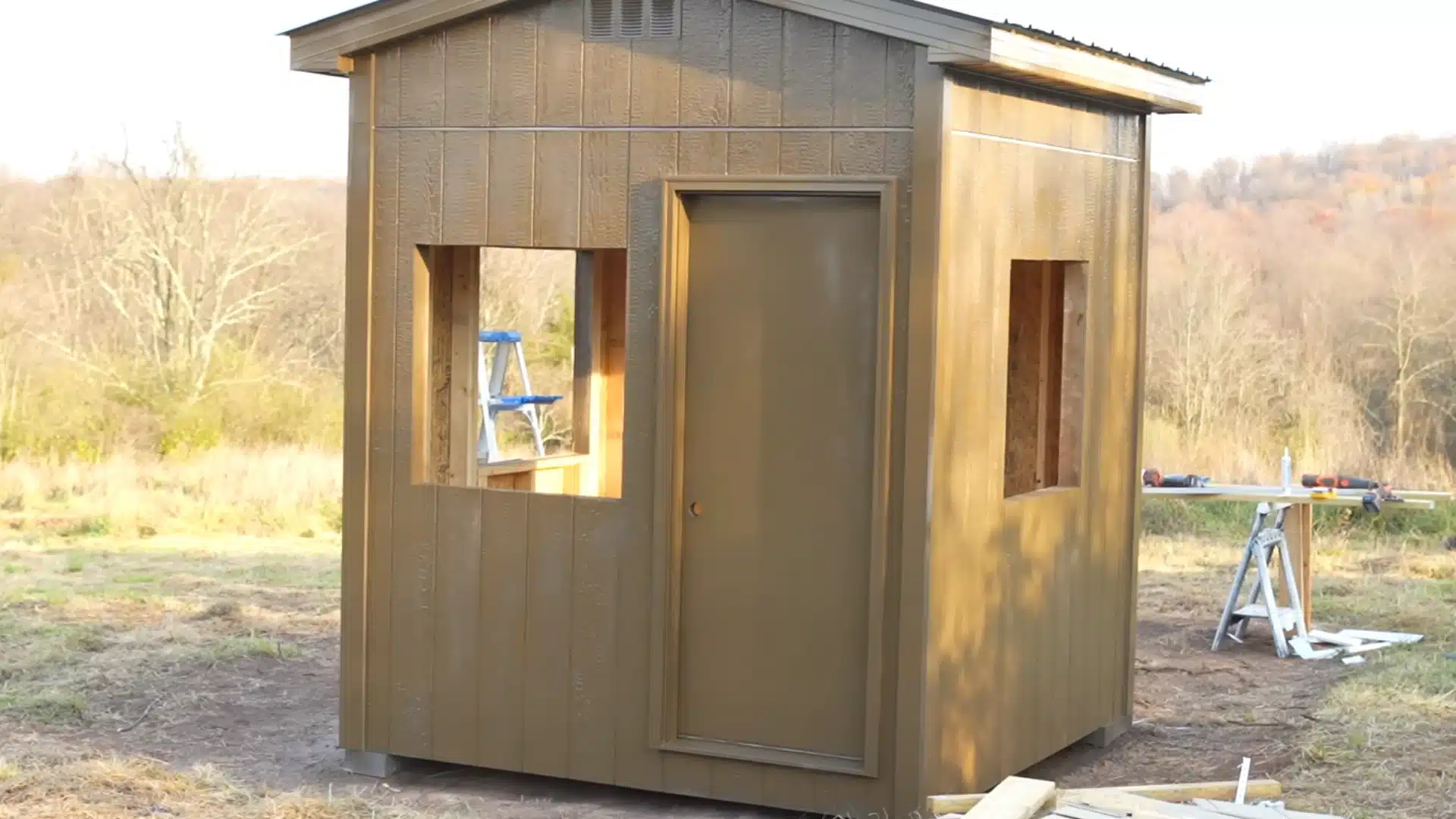 painting exterior walls of shed with brush along siding in warm daylight