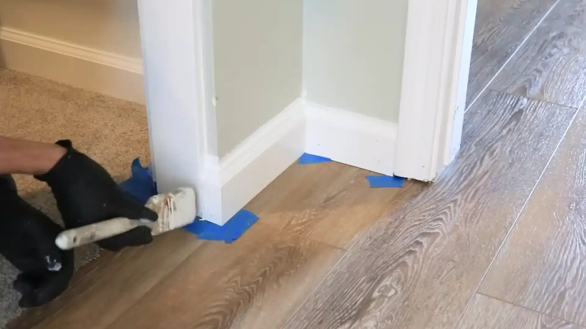person painting white baseboard trim along a doorway for a finished look
