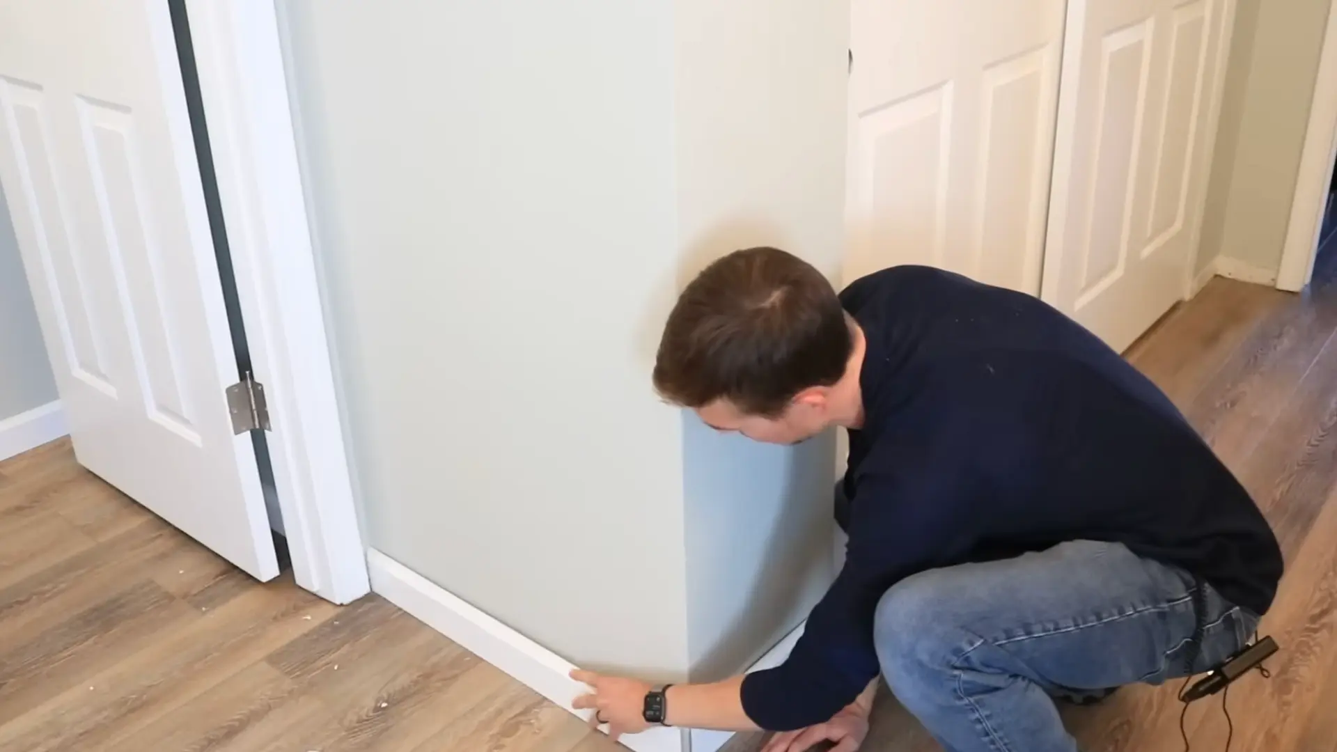 person positioning white baseboard trim along a wall corner before securing it