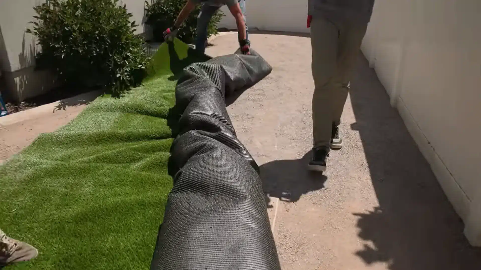 person rolling out artificial grass across a prepared backyard surface before securing the edges