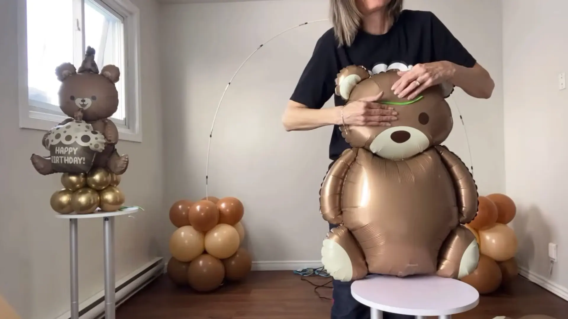 person securing a large teddy bear balloon on the balloon arch setup