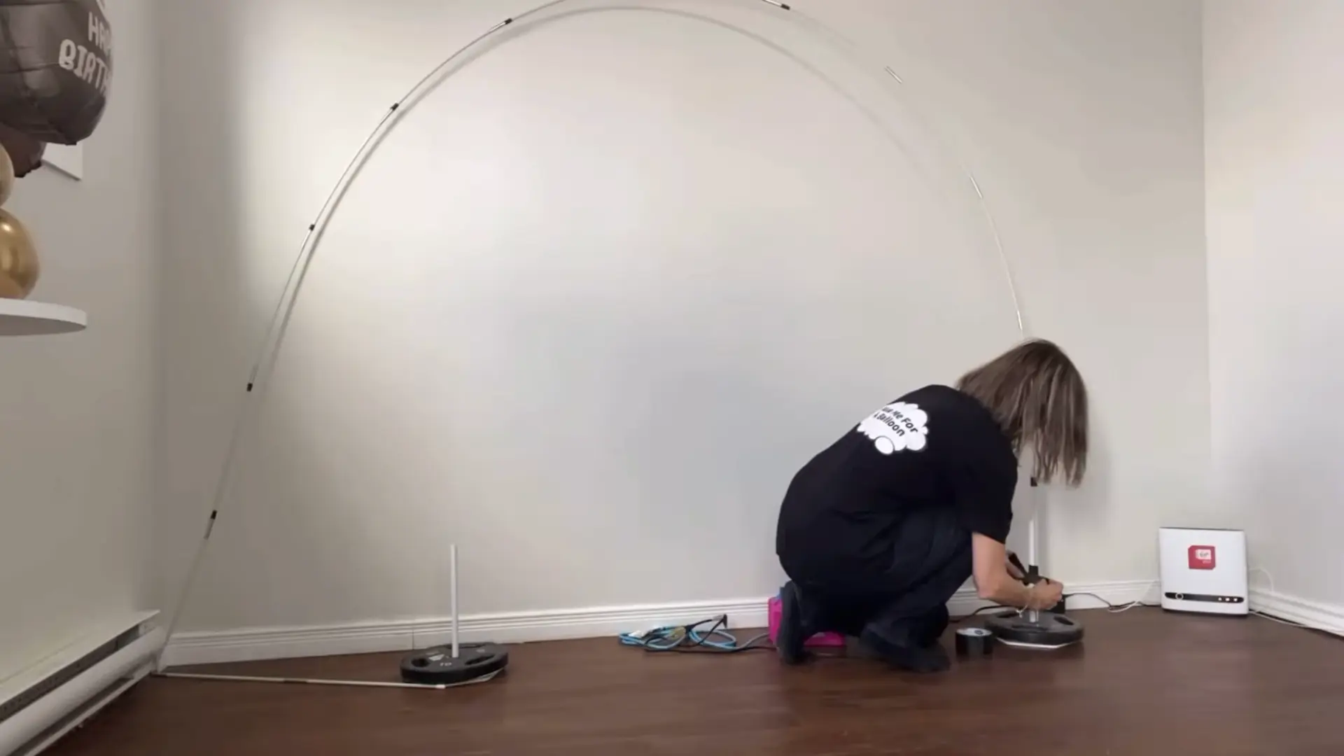 person securing the balloon arch stand base while adjusting the curved frame