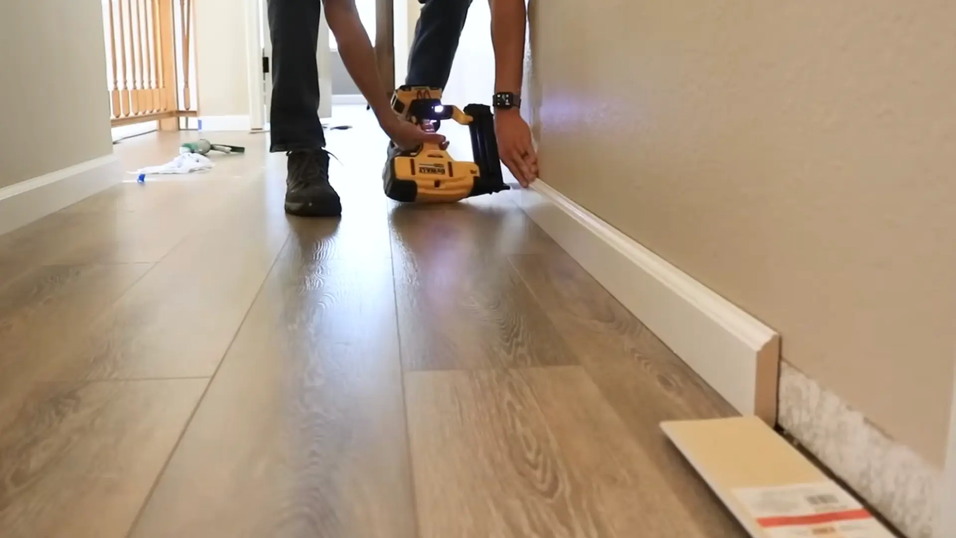 person securing white baseboard trim to a wall using a cordless nail gun