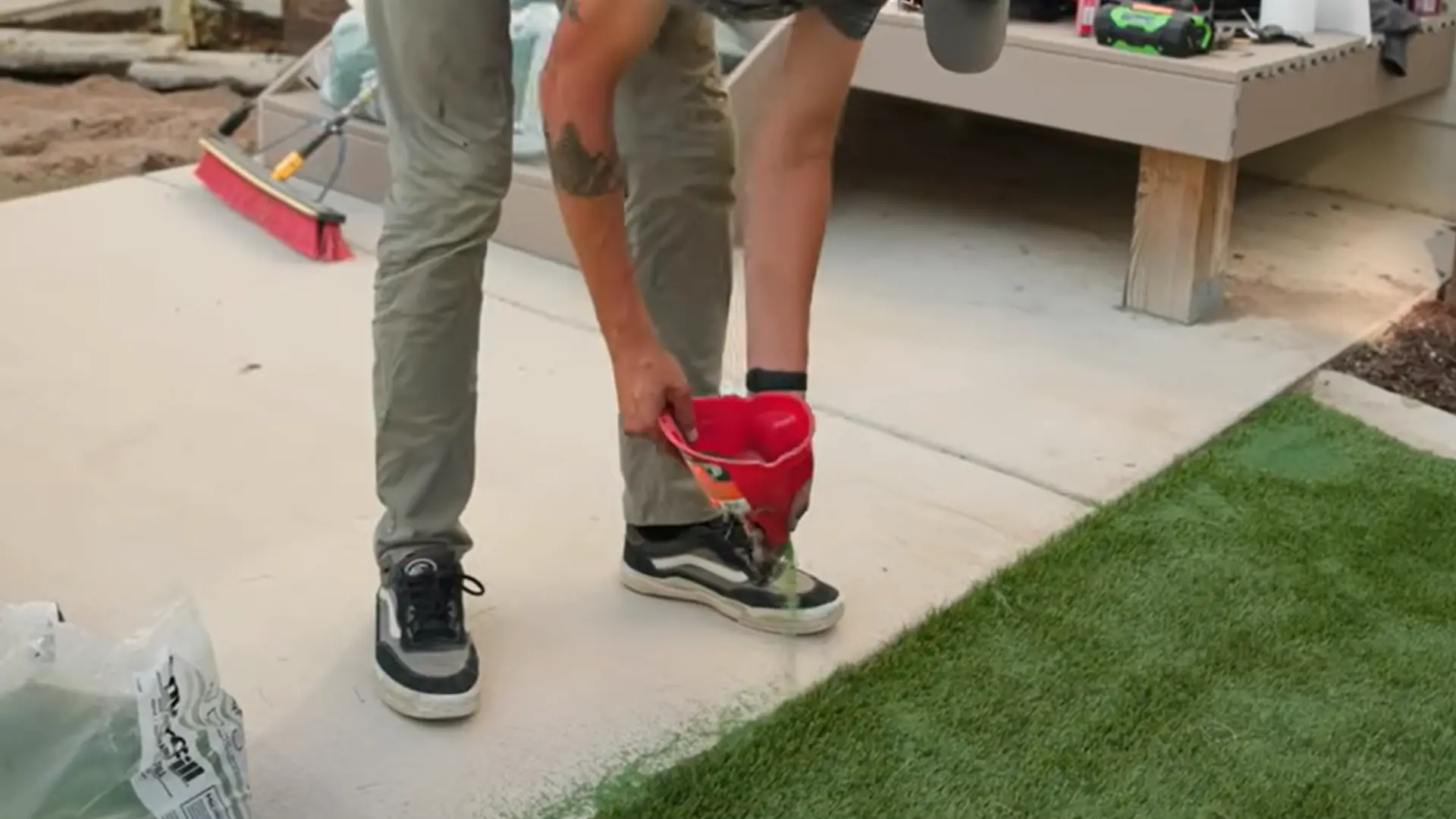 person spreading silica sand infill over artificial grass while brushing the fibers upright evenly