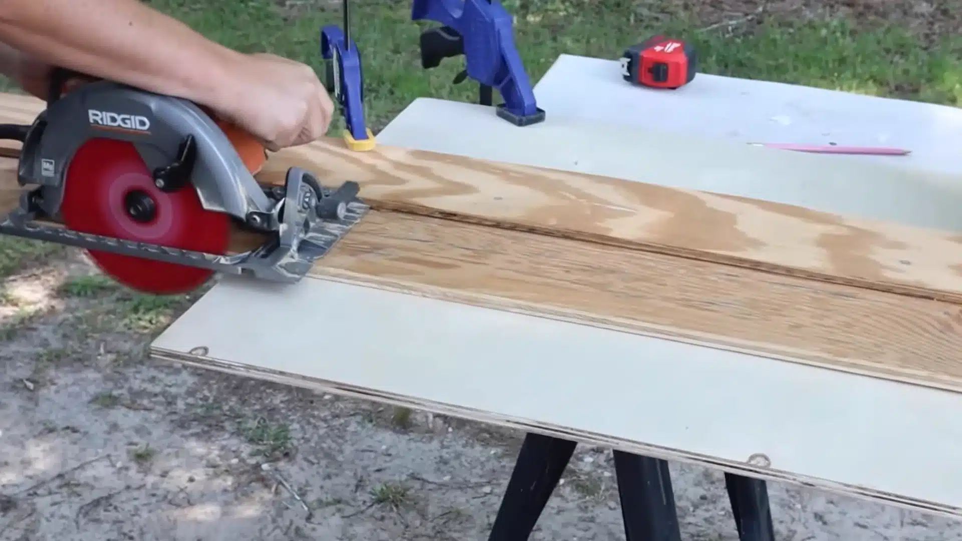 person using a circular saw to cut plywood boards clamped on a sawhorse work table outdoors