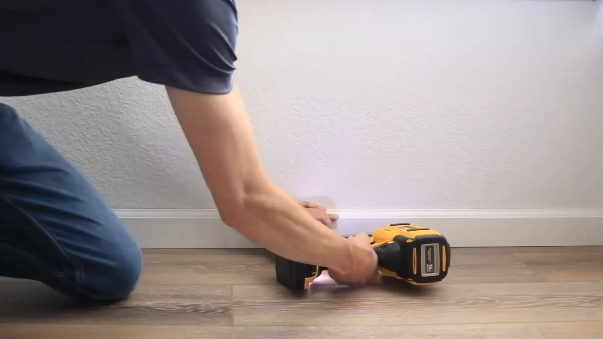 person using a power tool to secure baseboard against an uneven floor