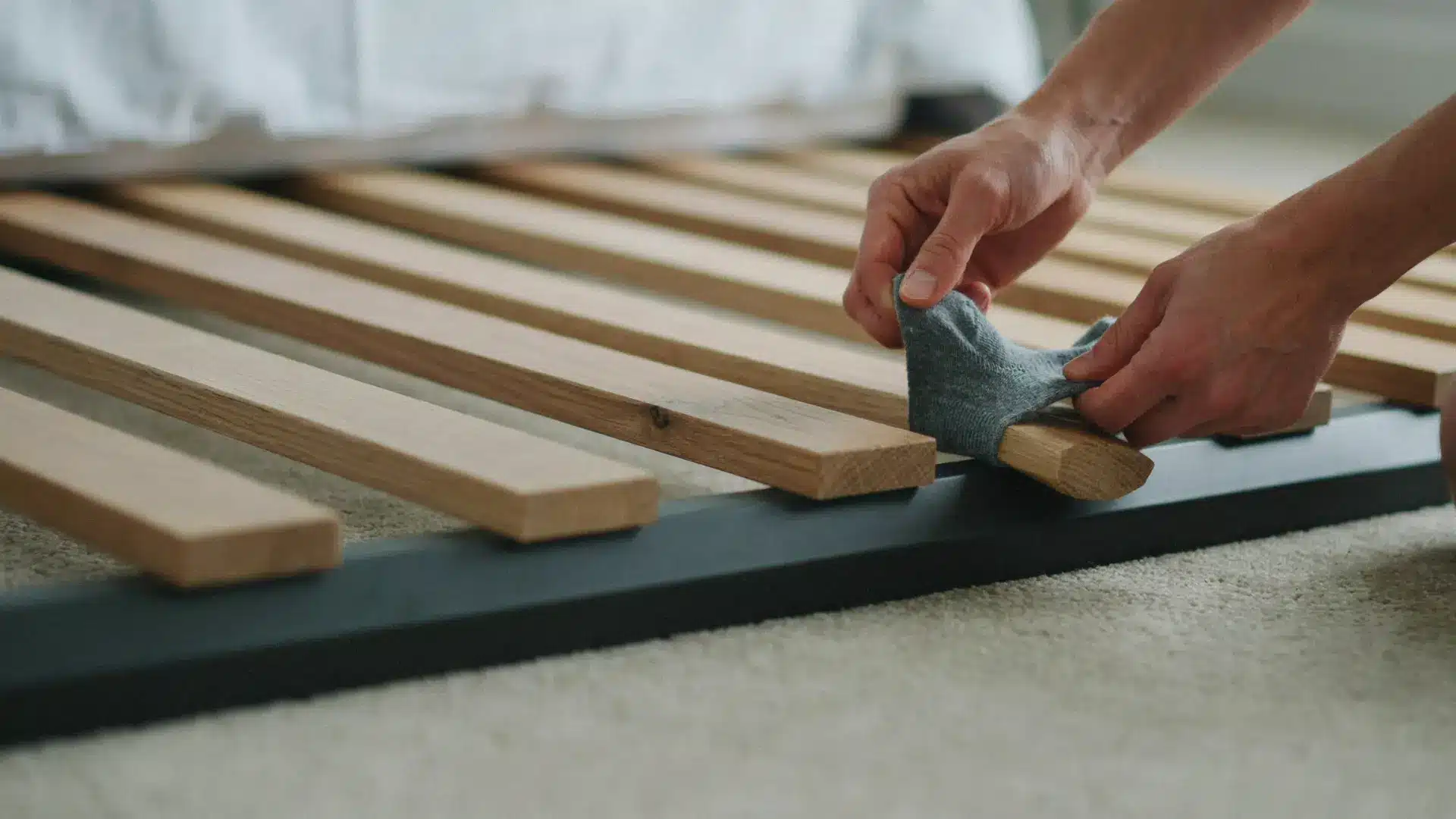 person wrapping cloth around a wooden bed slat to reduce friction and squeaks