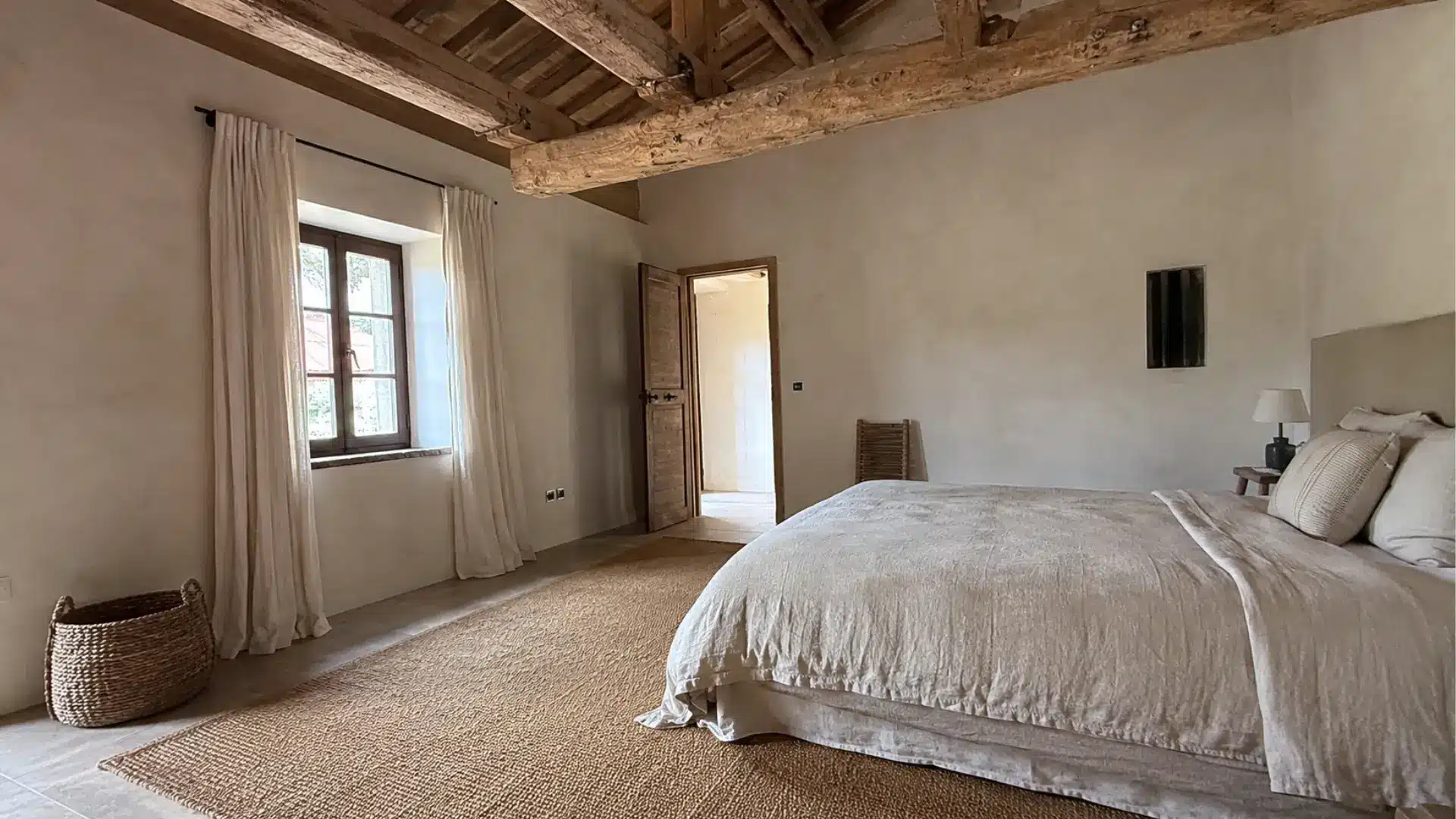 rustic neutral bedroom with exposed wood beams, jute rug, and linen bedding