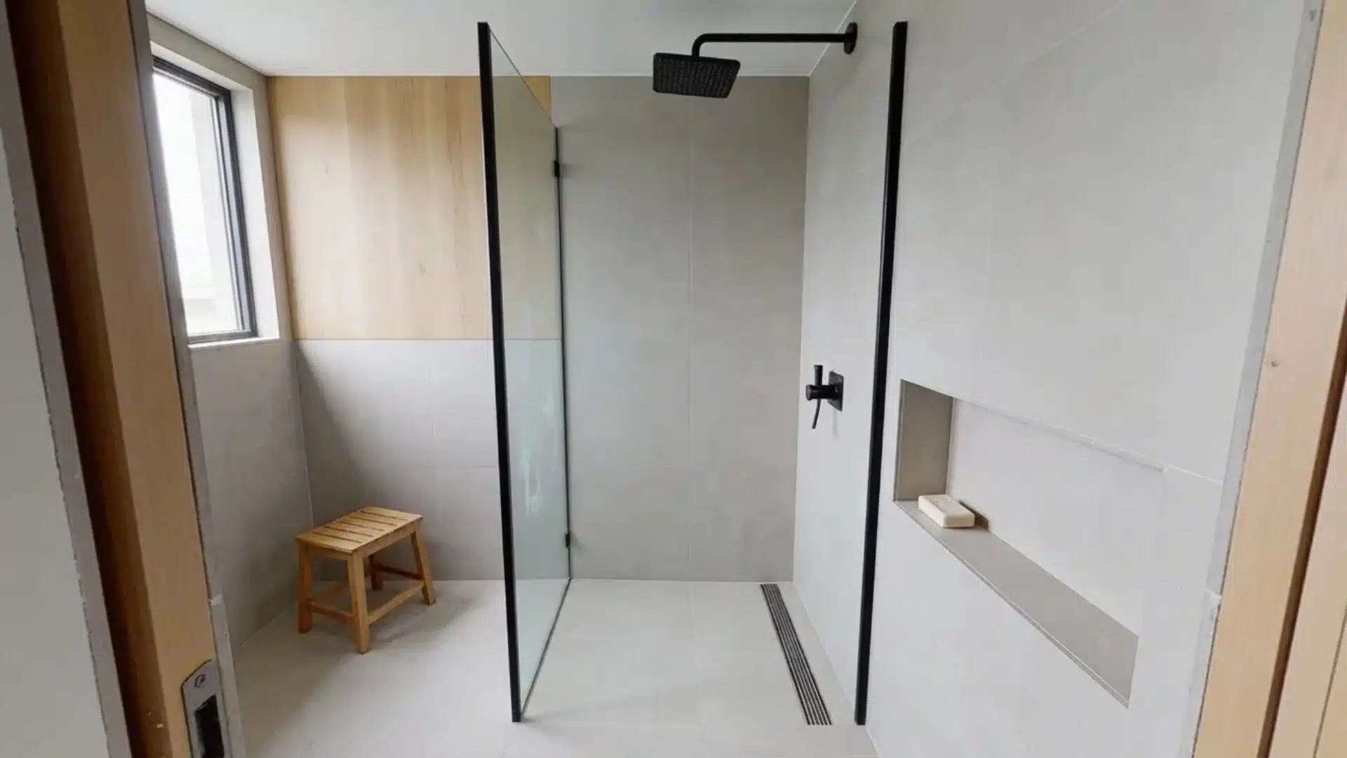 scandinavian style bathroom with gray tiles, a glass shower, black fixtures, and a wooden bench