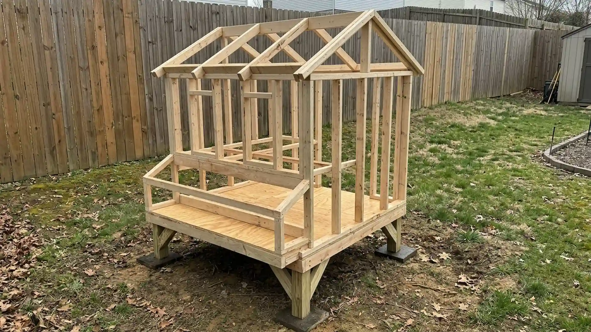 unfinished wooden chicken coop frame raised on posts in a backyard with a tall wooden privacy fences