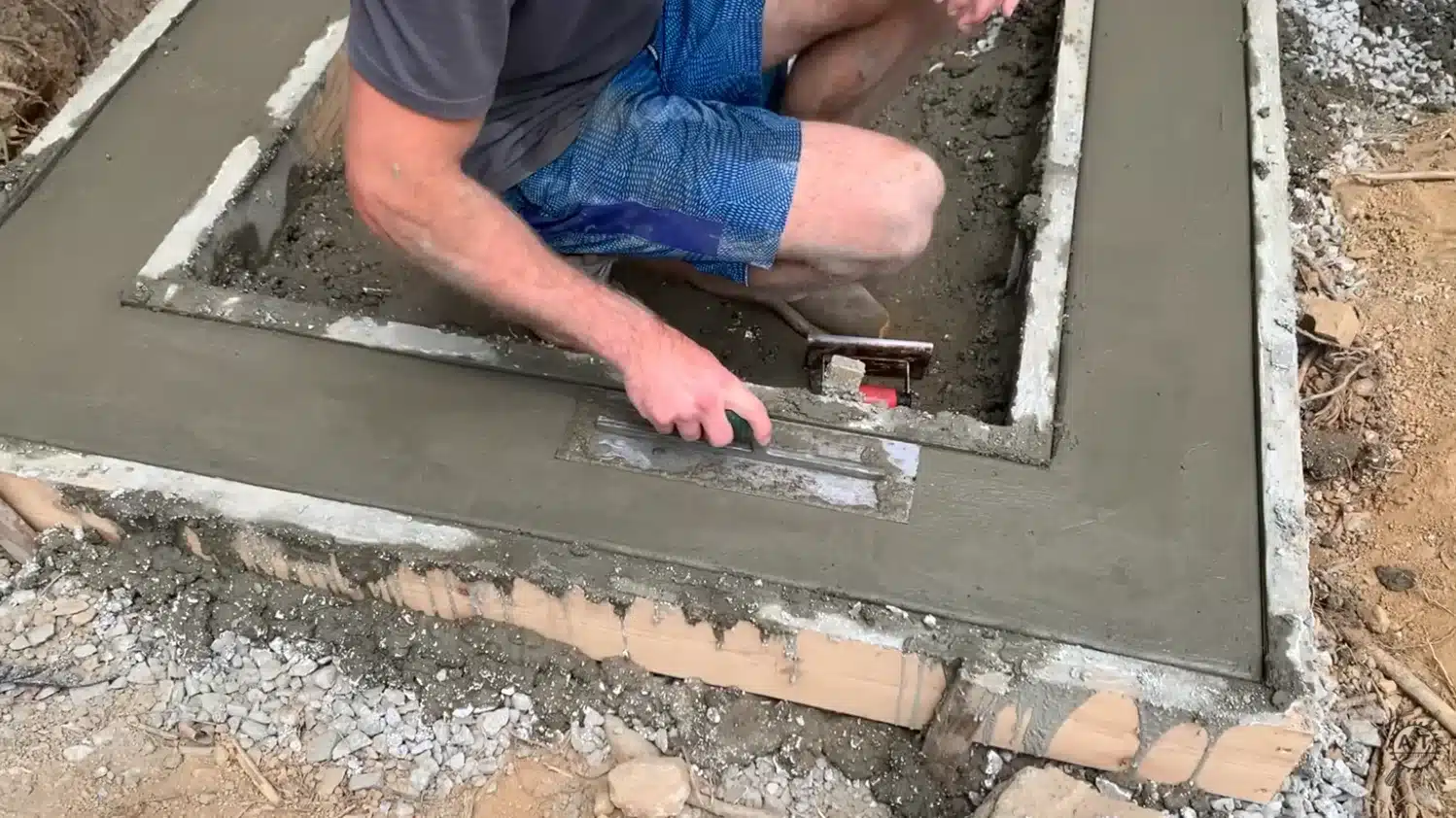 smoothing wet concrete with a hand trowel inside a wooden shower pan curb form now