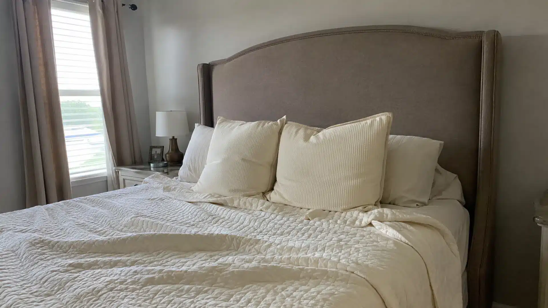 taupe upholstered wingback headboard with cream quilted bedding and corduroy pillows