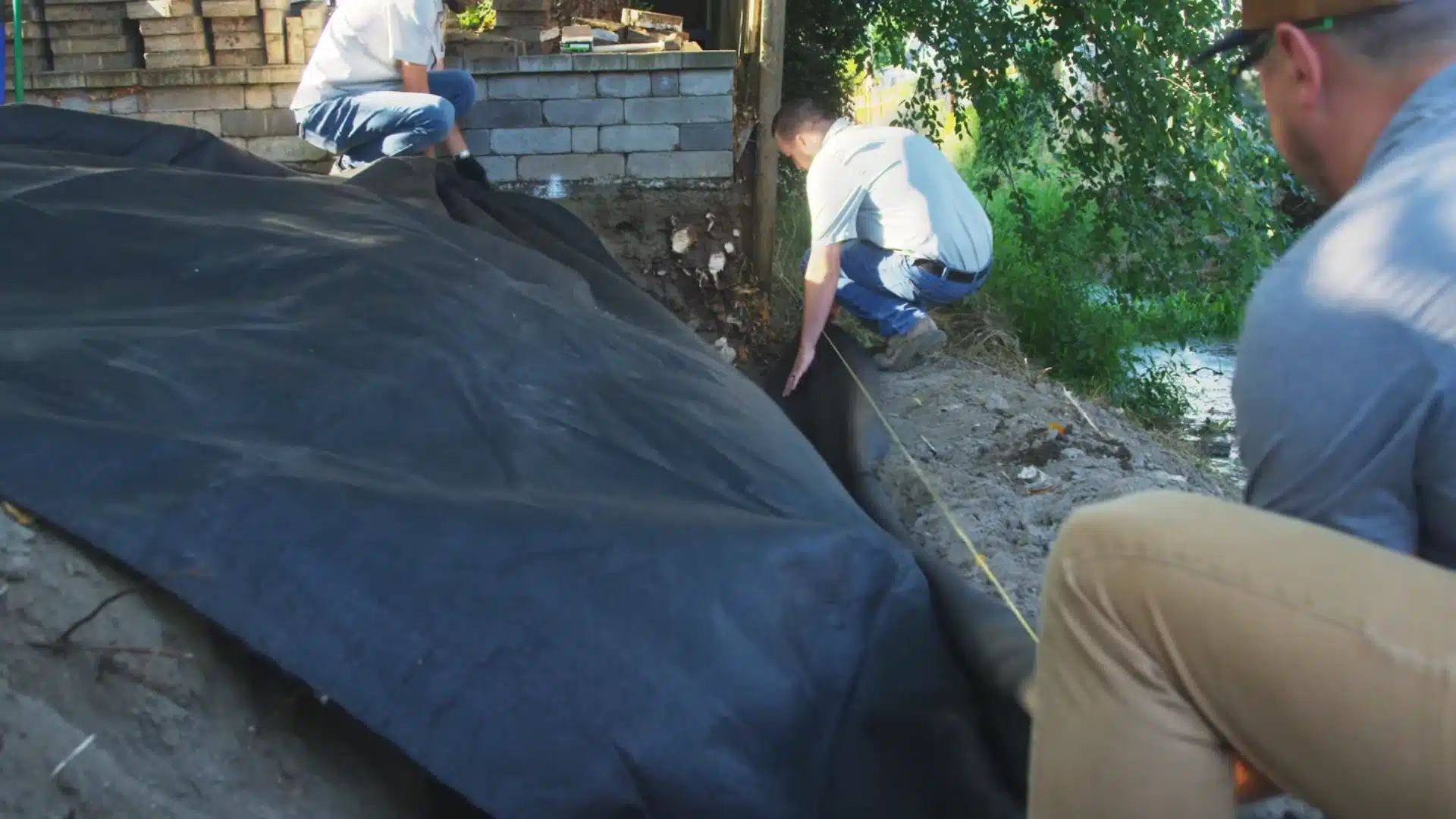 three workers measuring and preparing excavation area lined with landscape fabric