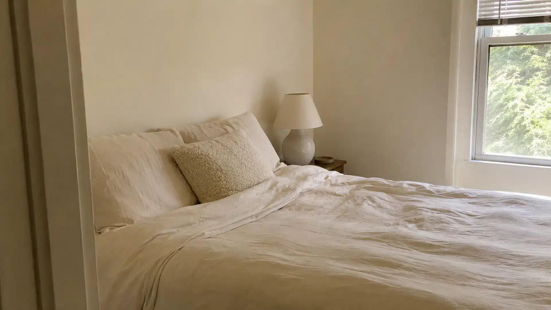 warm white monochrome bedroom with matte linen bedding and ceramic table lamp