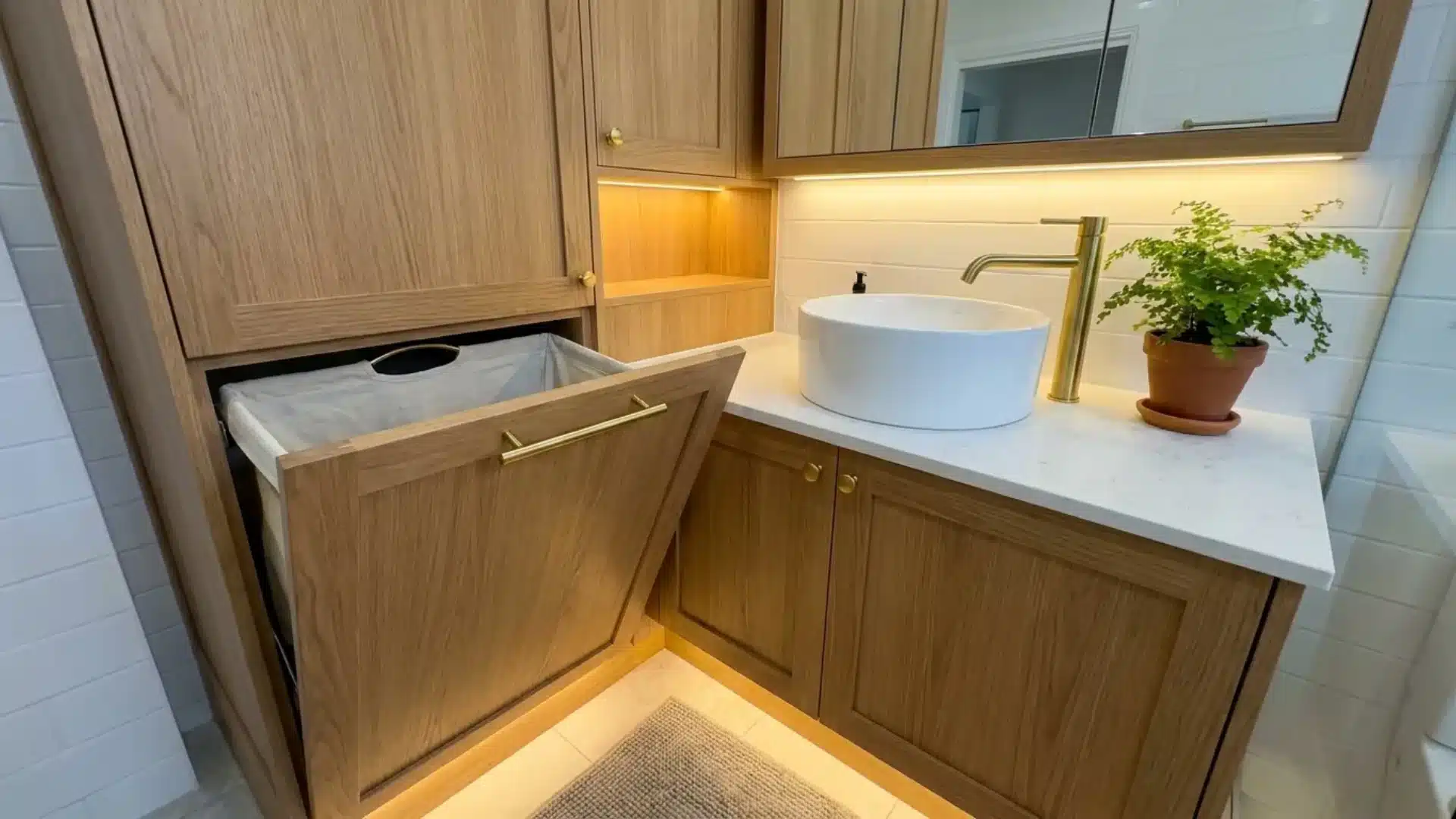 wood vanity with pull out laundry hamper open beside round sink and gold faucet