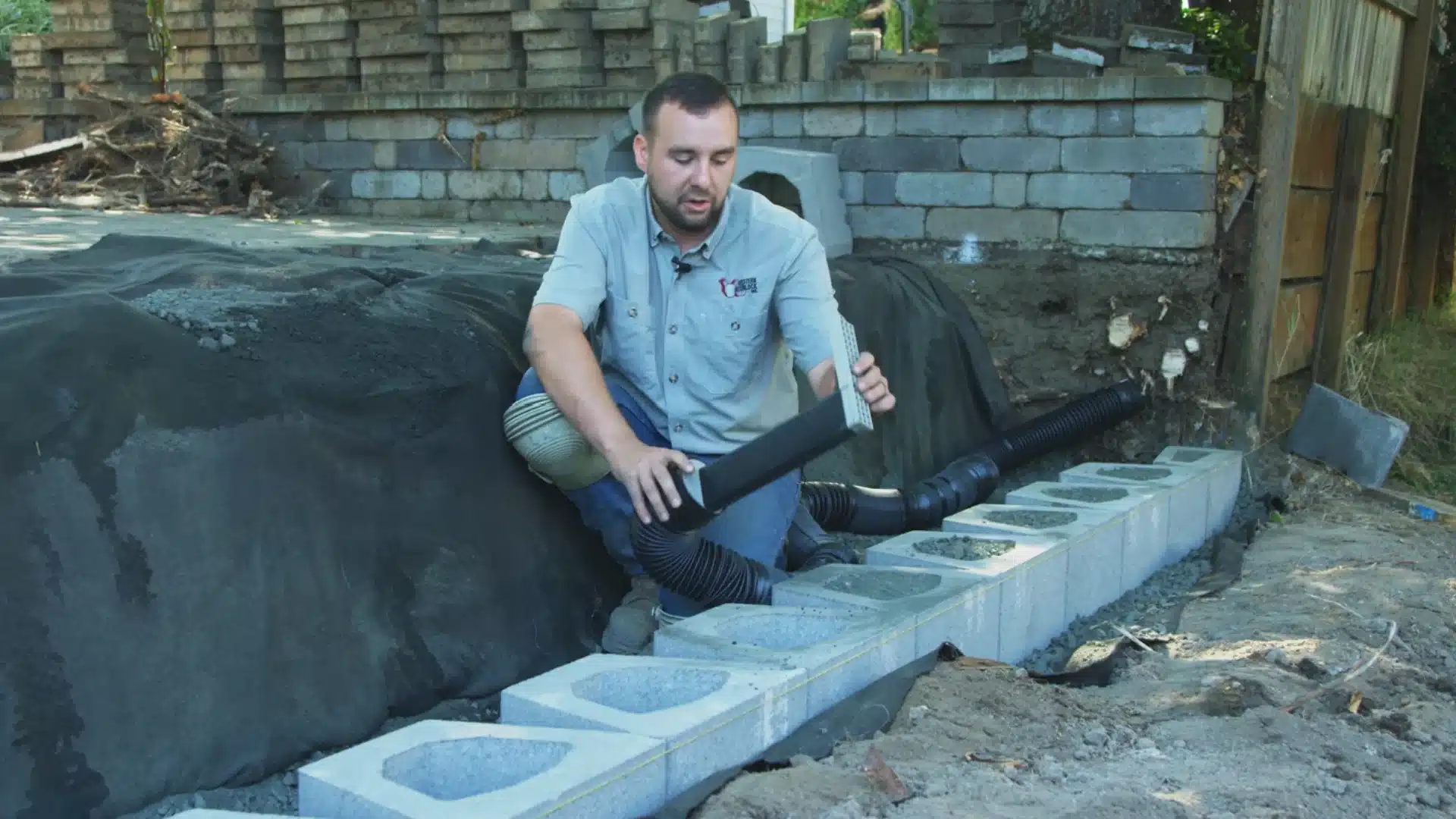 worker connecting a perforated drain pipe fitting to base course wall blocks