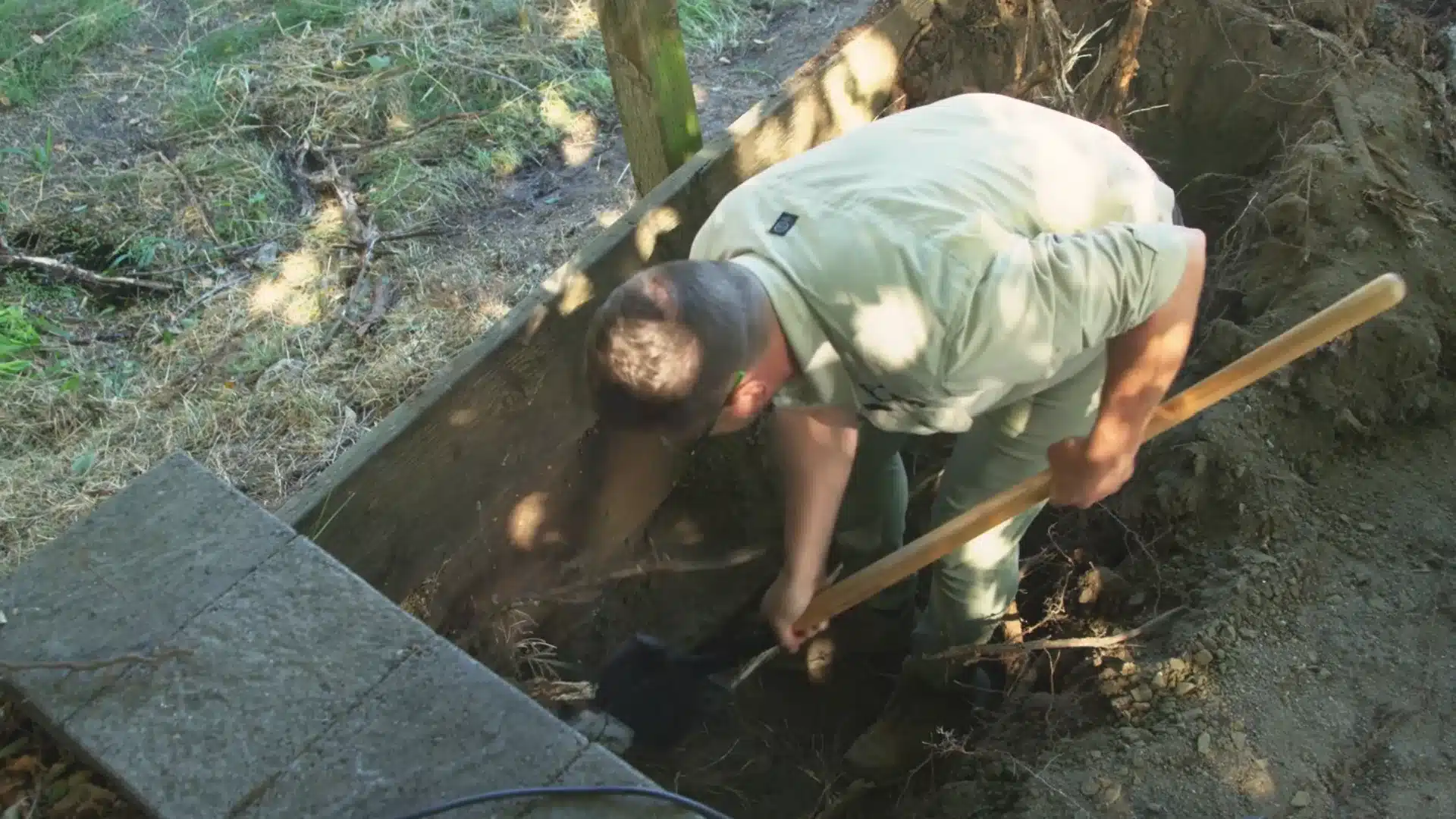worker digging excavation trench for retaining wall base with a shovel