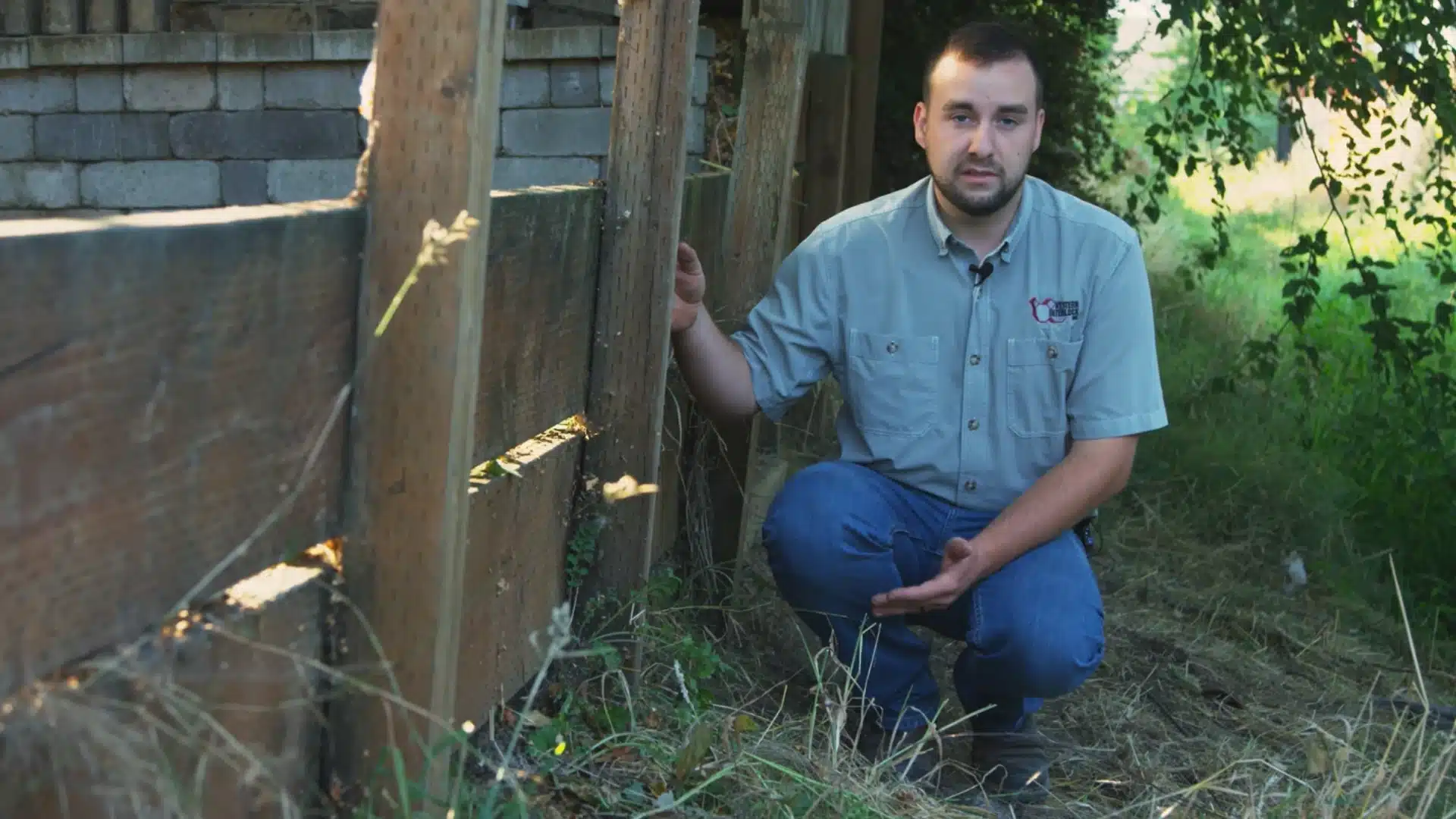 worker kneeling beside an old failing wood retaining wall inspecting the structure