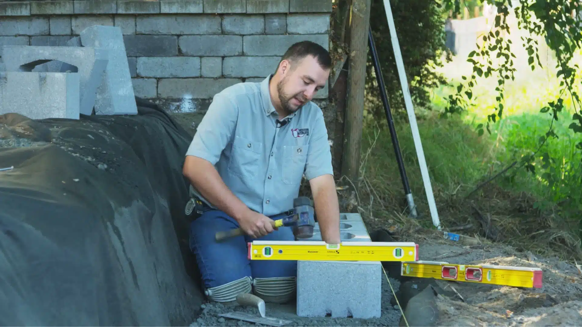 worker leveling a concrete retaining wall block with a rubber mallet and spirit level