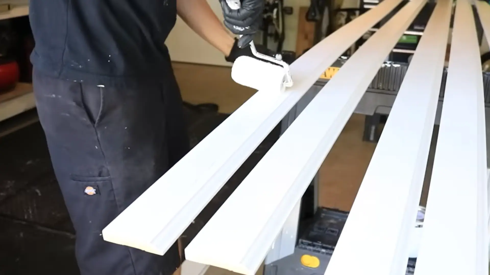 worker rolling white paint onto baseboard trim before installation