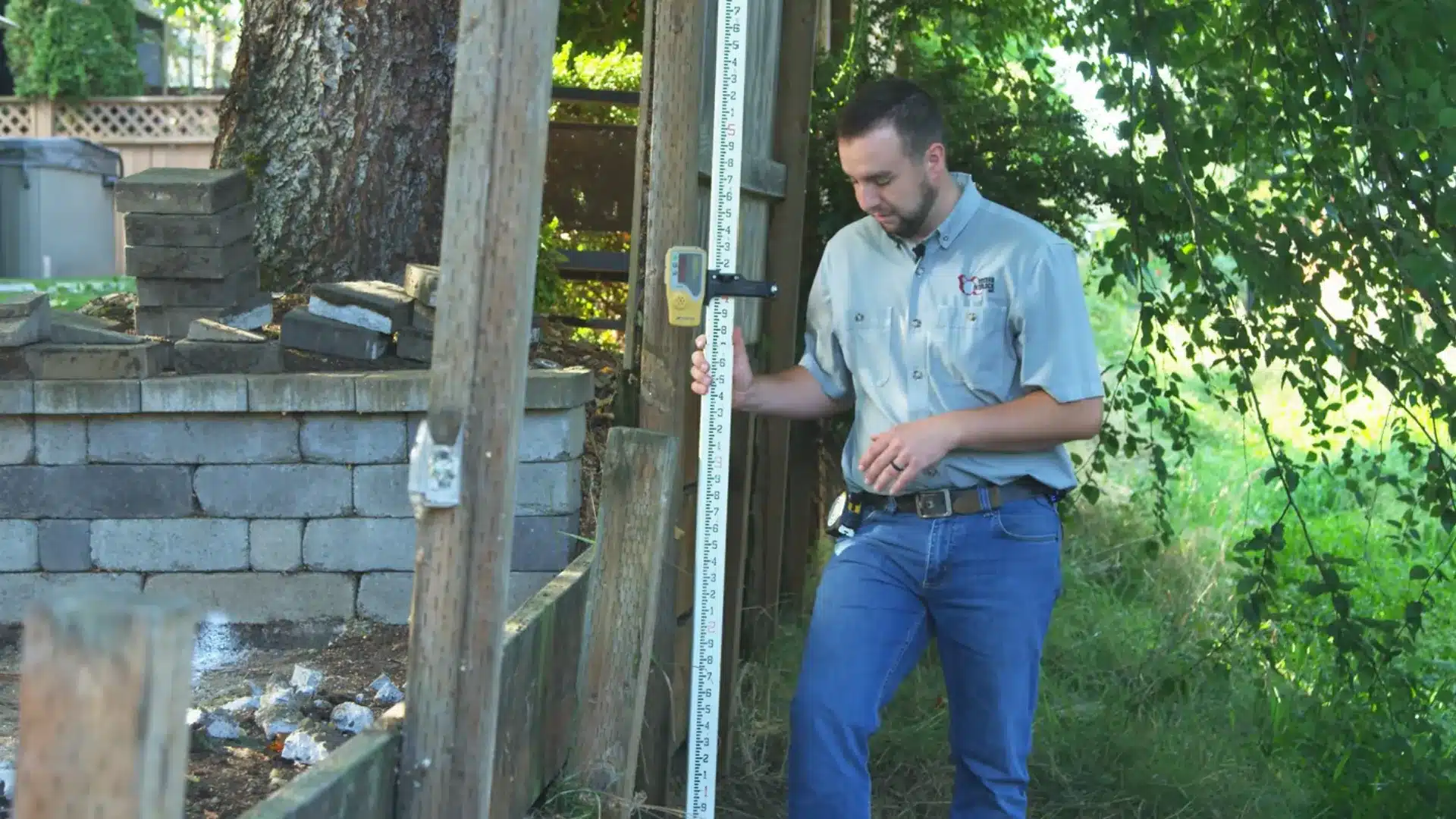 worker using a laser level and measuring rod to set finish grade height for the retaining wall