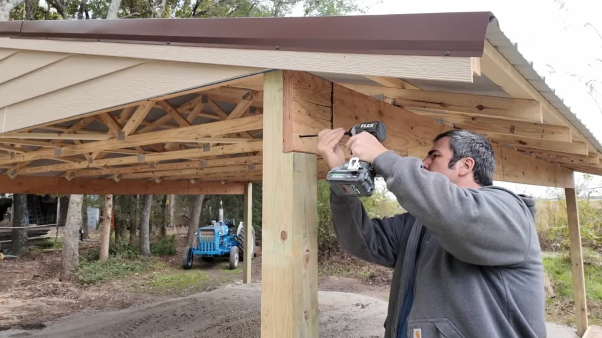 man using a drill to attach trim boards under a carport roof with visible trusses