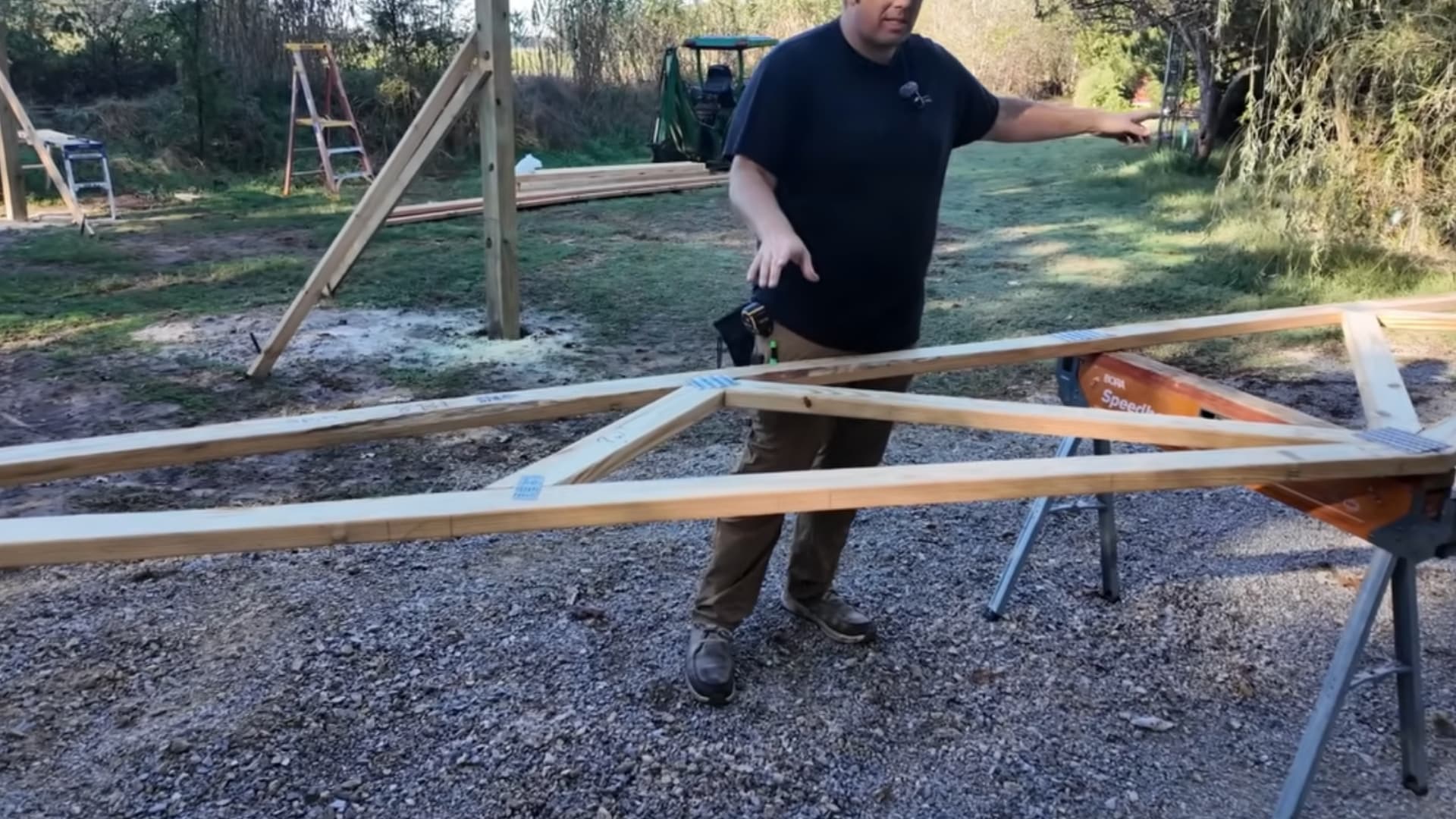 man standing beside a large wooden gable truss assembled flat on the ground at a build site