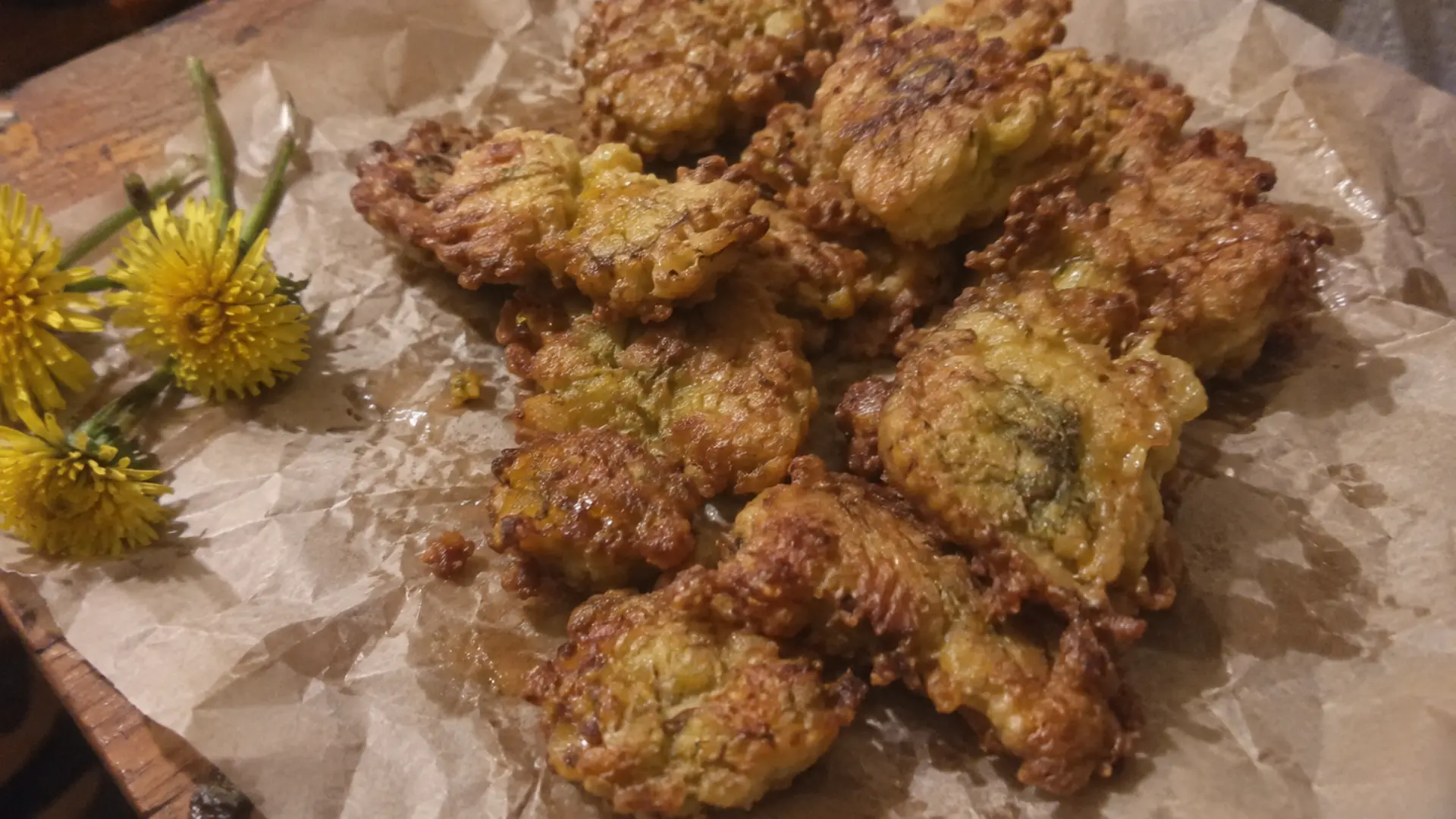 golden dandelion fritters on parchment paper with fresh yellow blooms nearby