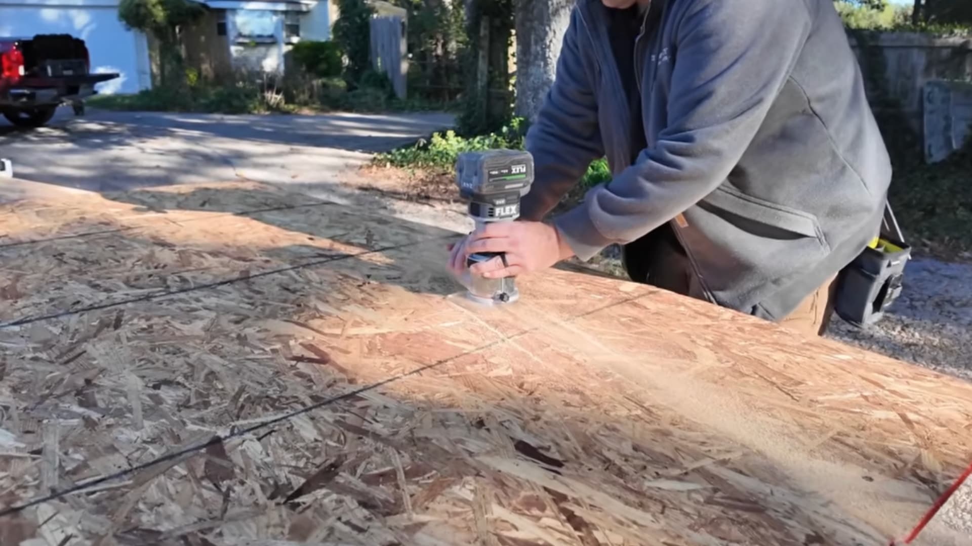 man using a handheld power tool to cut along marked guide lines on a large plywood roof sheathing panel