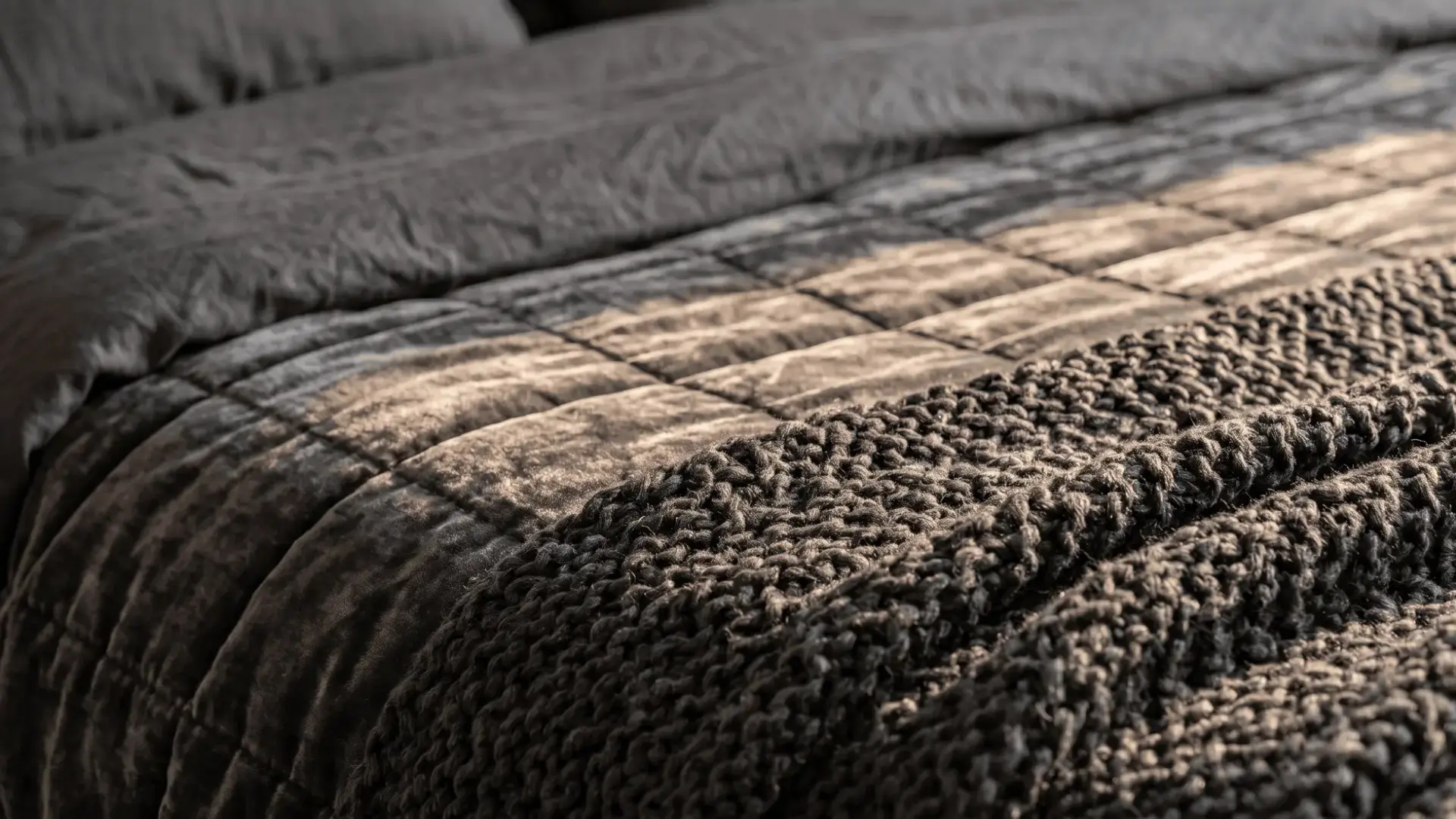 layered bedding with velvet and chunky knit textures in charcoal tones for a cozy bedroom look